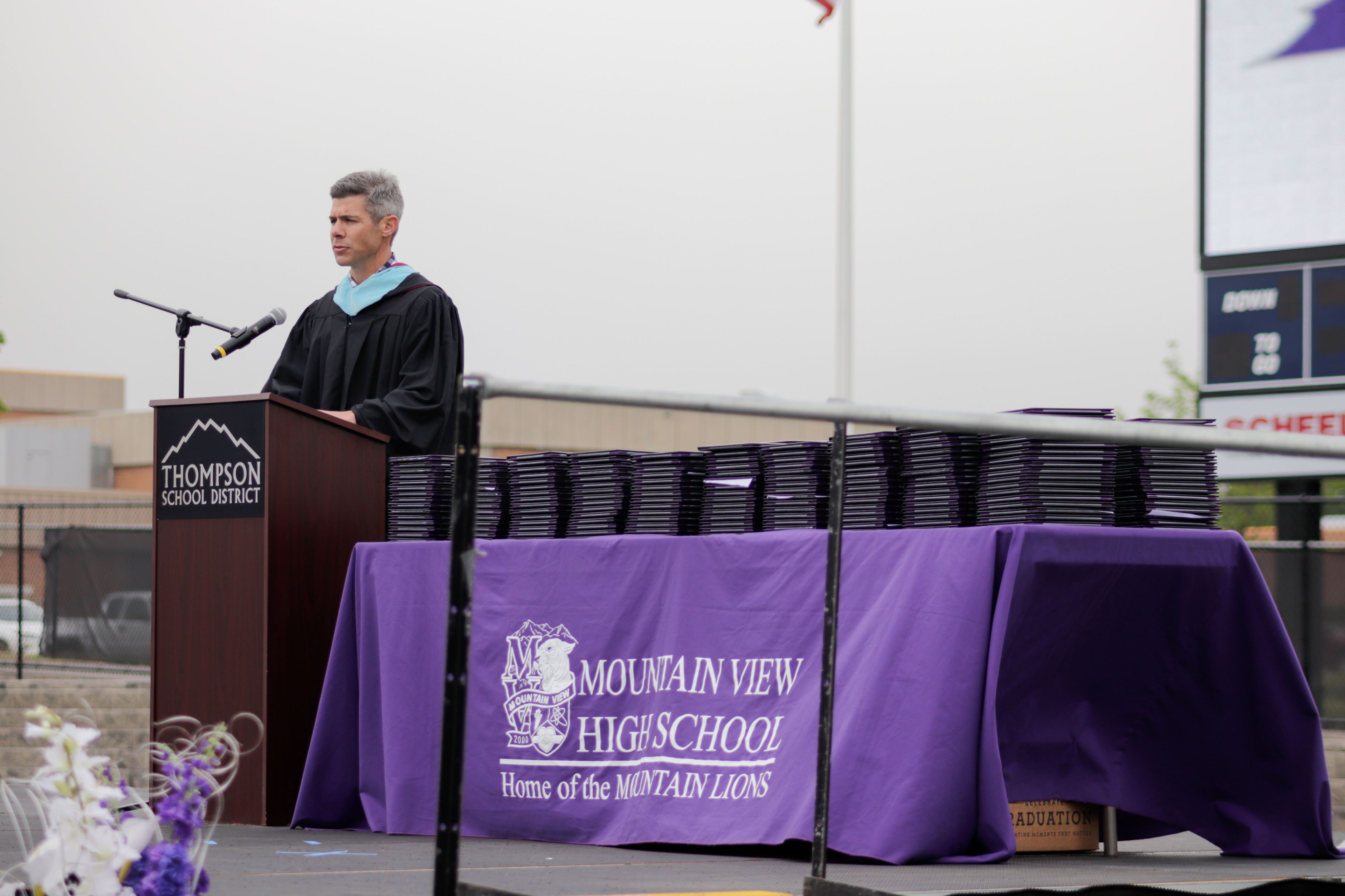 LOVELAND, CO - MAY 29, 2021: Mountain View Assistant Principal and Staff Speaker Nathan Gurrini speaks of the lessons high school students learn outside of class, including time management and responsibility, during the graduation ceremony Saturday, May 29, 2021 at Patterson Field in Loveland. (Michael Marquardt/Loveland Reporter-Herald)