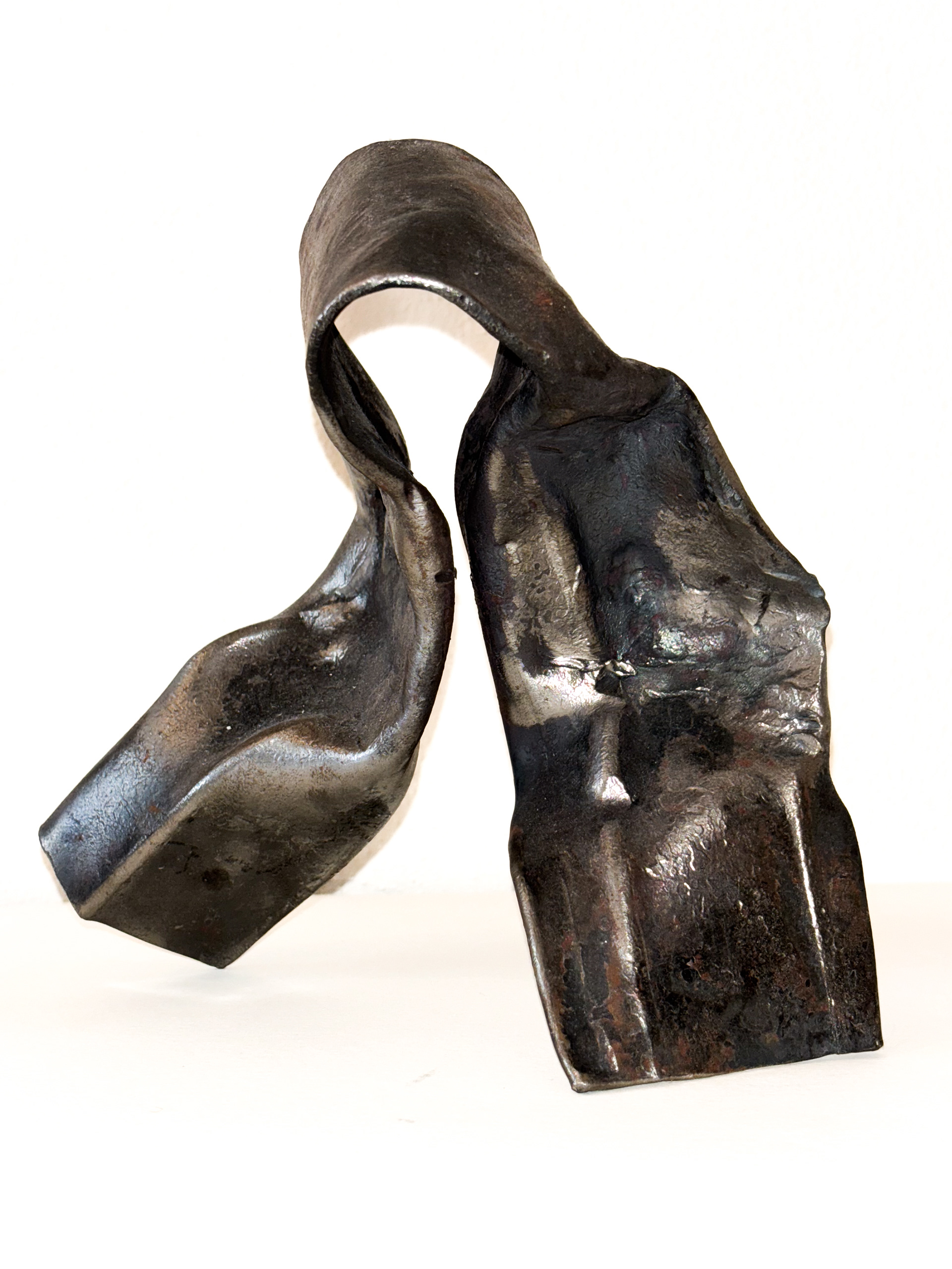 Geschmiedetes Kunstwerk aus Eisen mit einer stark gebogenen Form. Die Oberfläche weist rauhe, metallische Strukturen auf und das Werk hat einen organischen, fließenden Charakter.