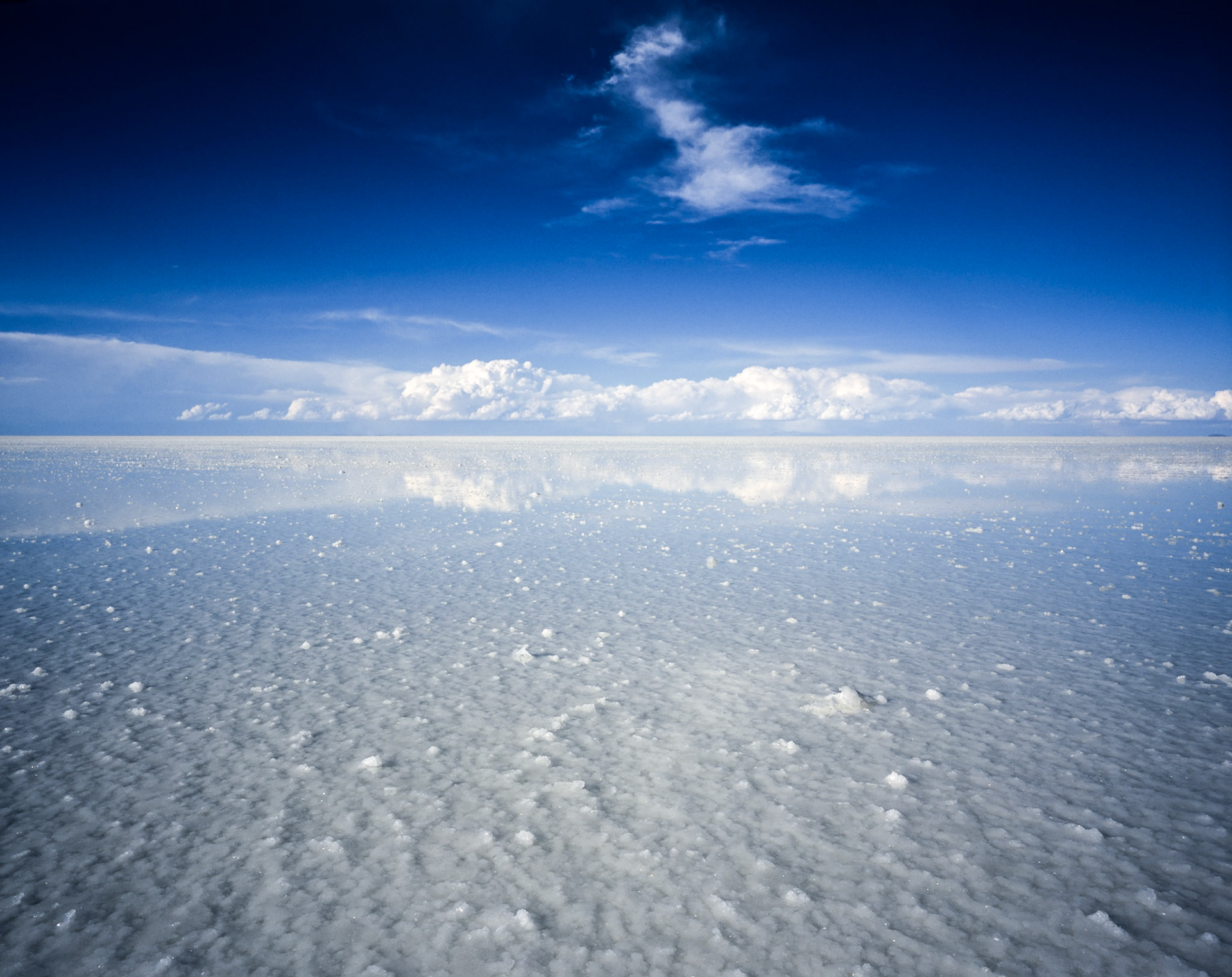 Thin layer of water, reflecting image of cloud, covering salt flats with blue sky and clouds in the distance at Salar de Uyuni, Bolivia