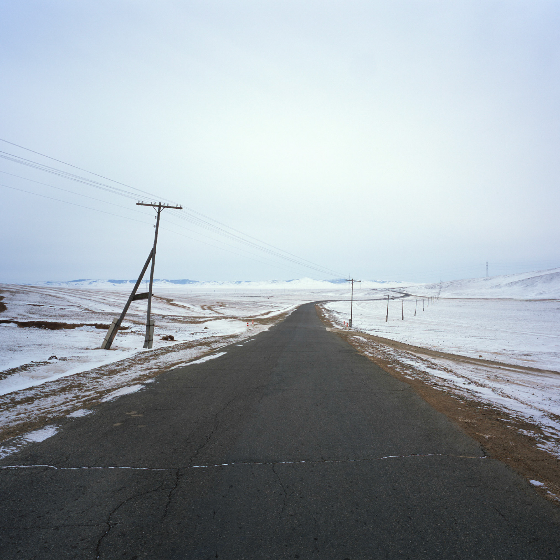 Telegraph poles and cables crossing an empty road in lightly snow covered Gorkhi Terelj National Park in Mongolia