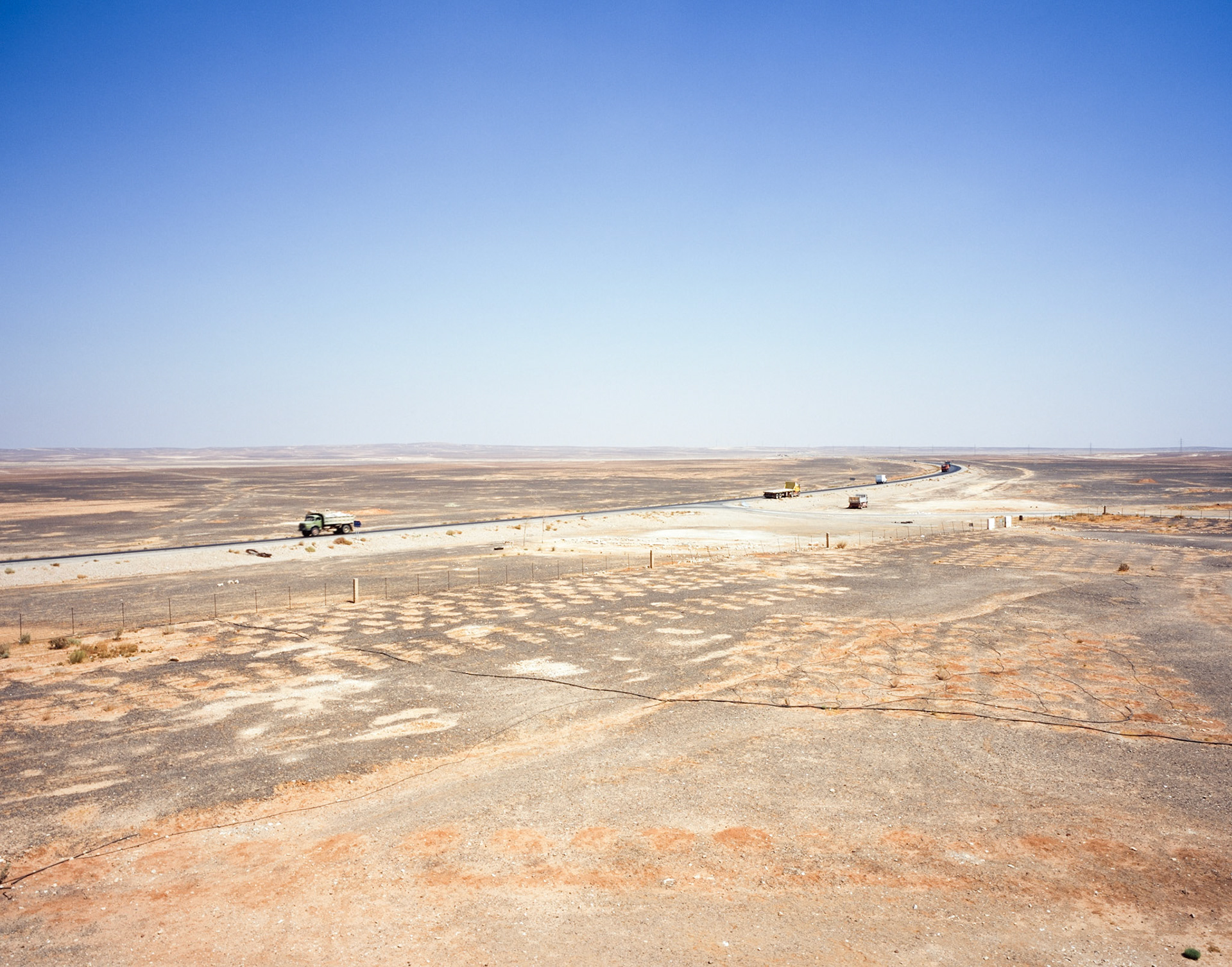 Trucks driving on isolated road in desert plain with cloudless sky overhead, Jordan