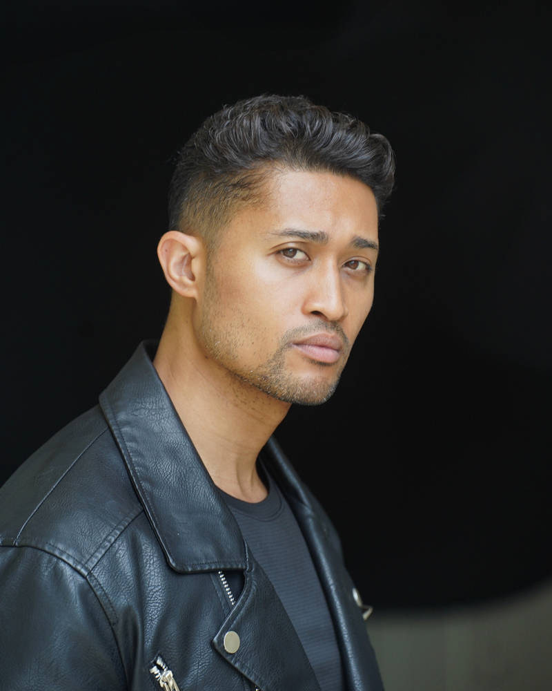 Man wearing a black leather jacket with a serious expression against a dark background