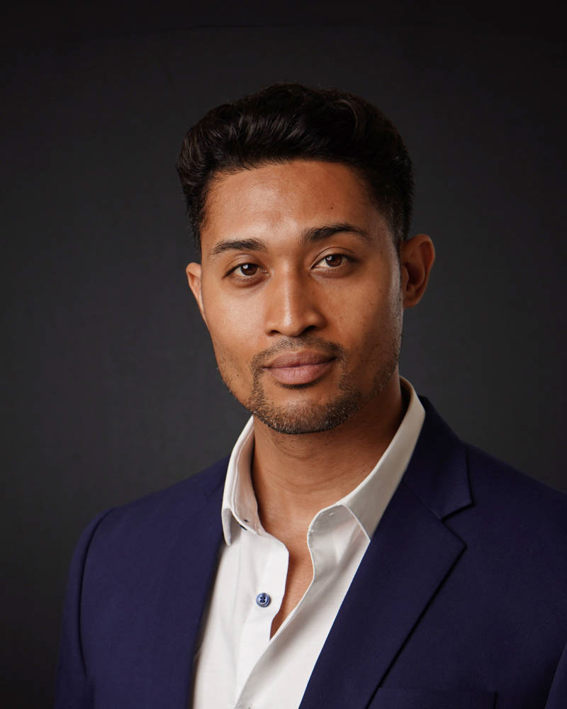 Professional studio headshot of a man in a navy blazer and white shirt against a dark background