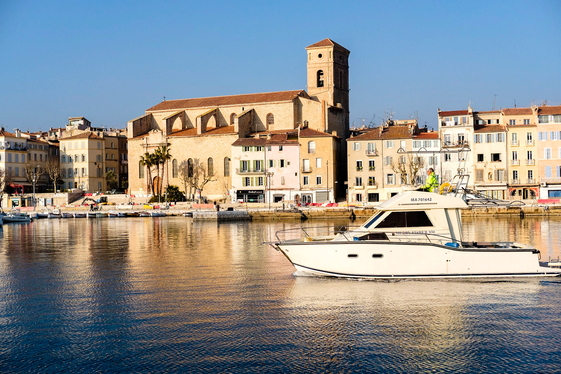 Un petit yacht entre dans le port de La Ciotat, dans le fond l'Église Notre-Dame-de-l'Assomption.