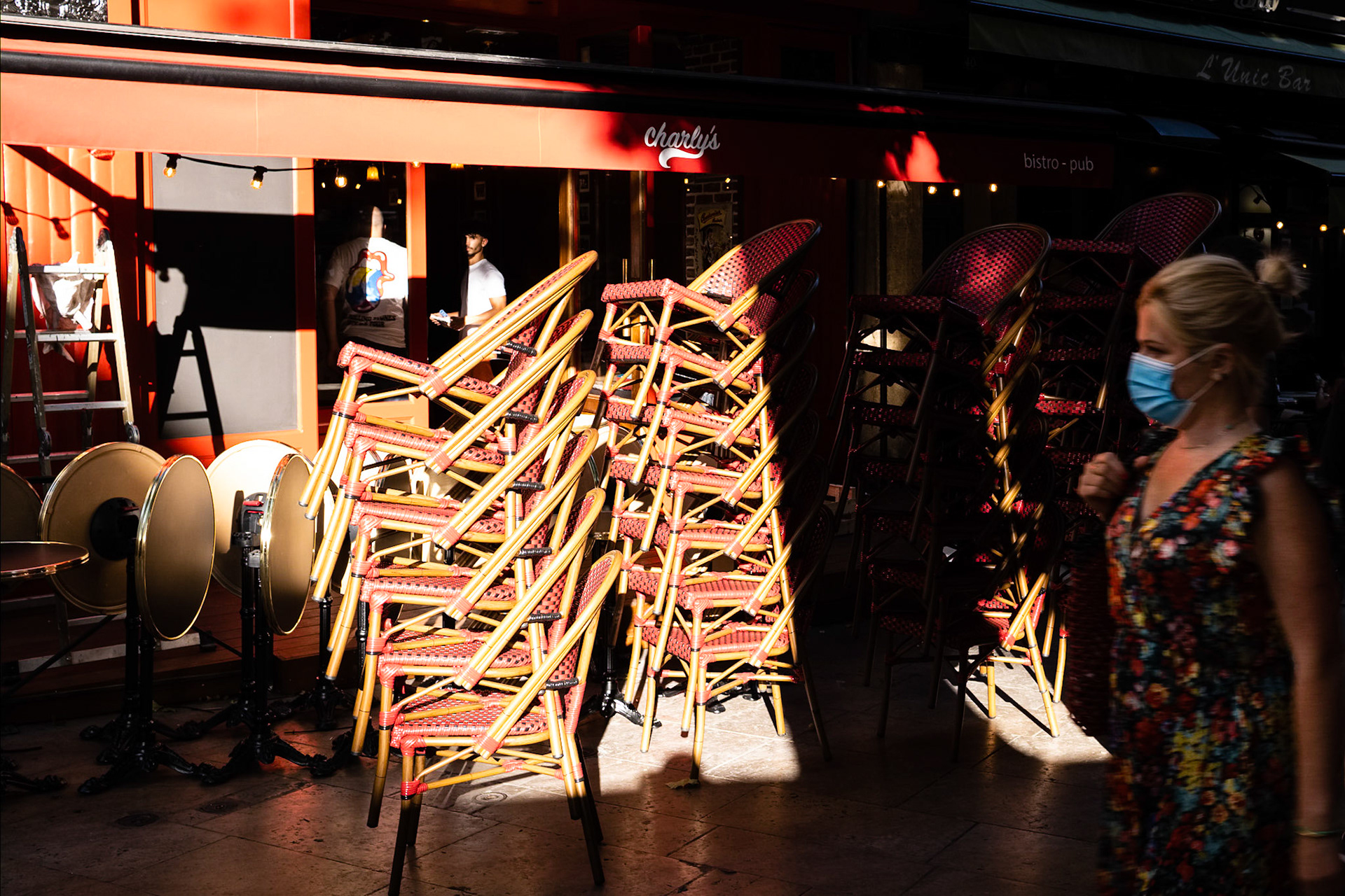 Aix en Provence, au temps du Covid-19. Une femme avec un masque passe devant un bar restaurant fermé, les chaises sont empilées.