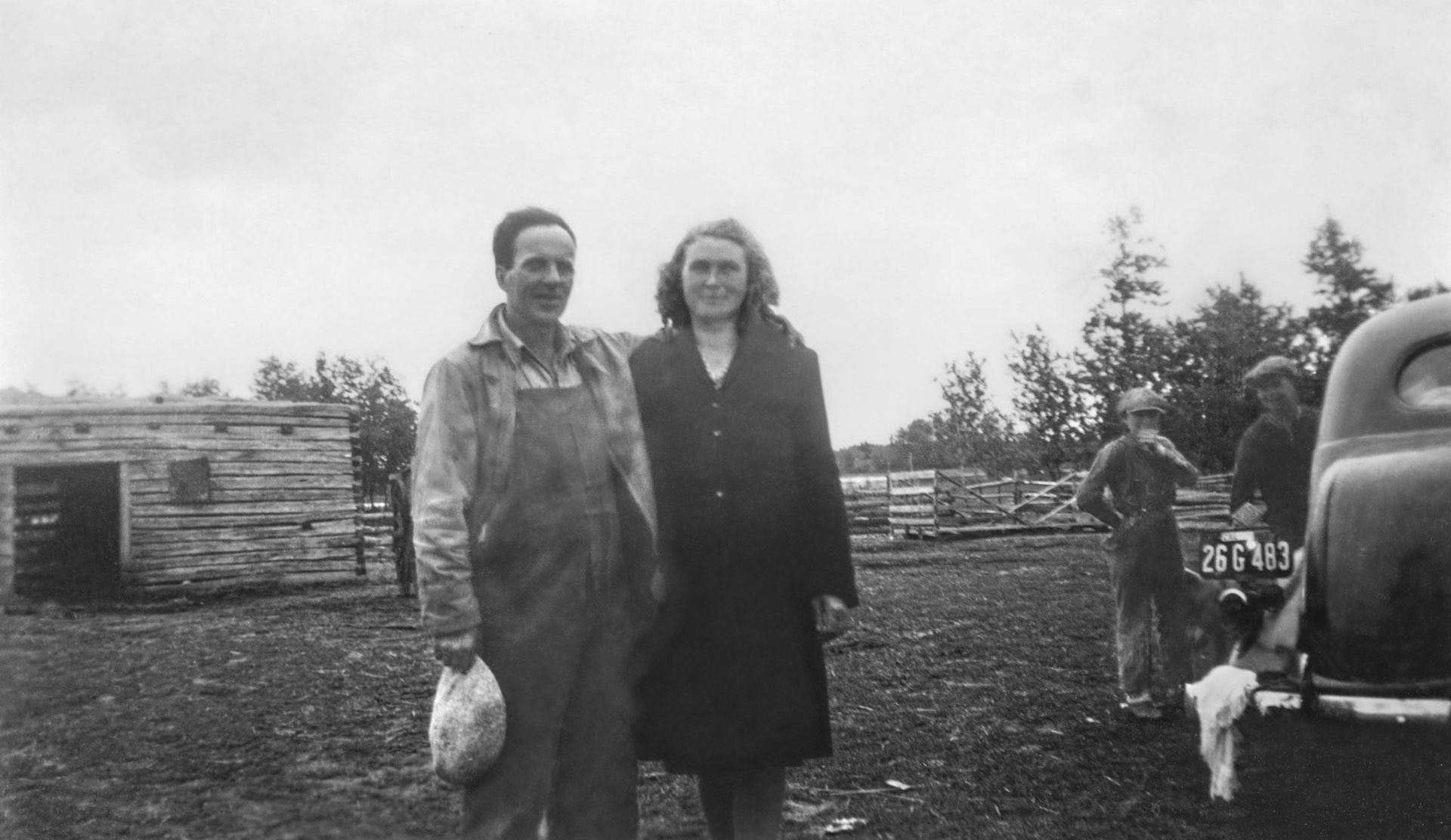 Circa 1945: John Huculak SR and wife Annie [Davie] Huculak on their famiky farm northeast of Willingdon, AB. Two male children in background are likely not brothers John and George Huculak (children of John and Doris) as one of the two male children can be seen peeking out behiind the car in a separate photo taken at same time and location. Unknown who the boys are.