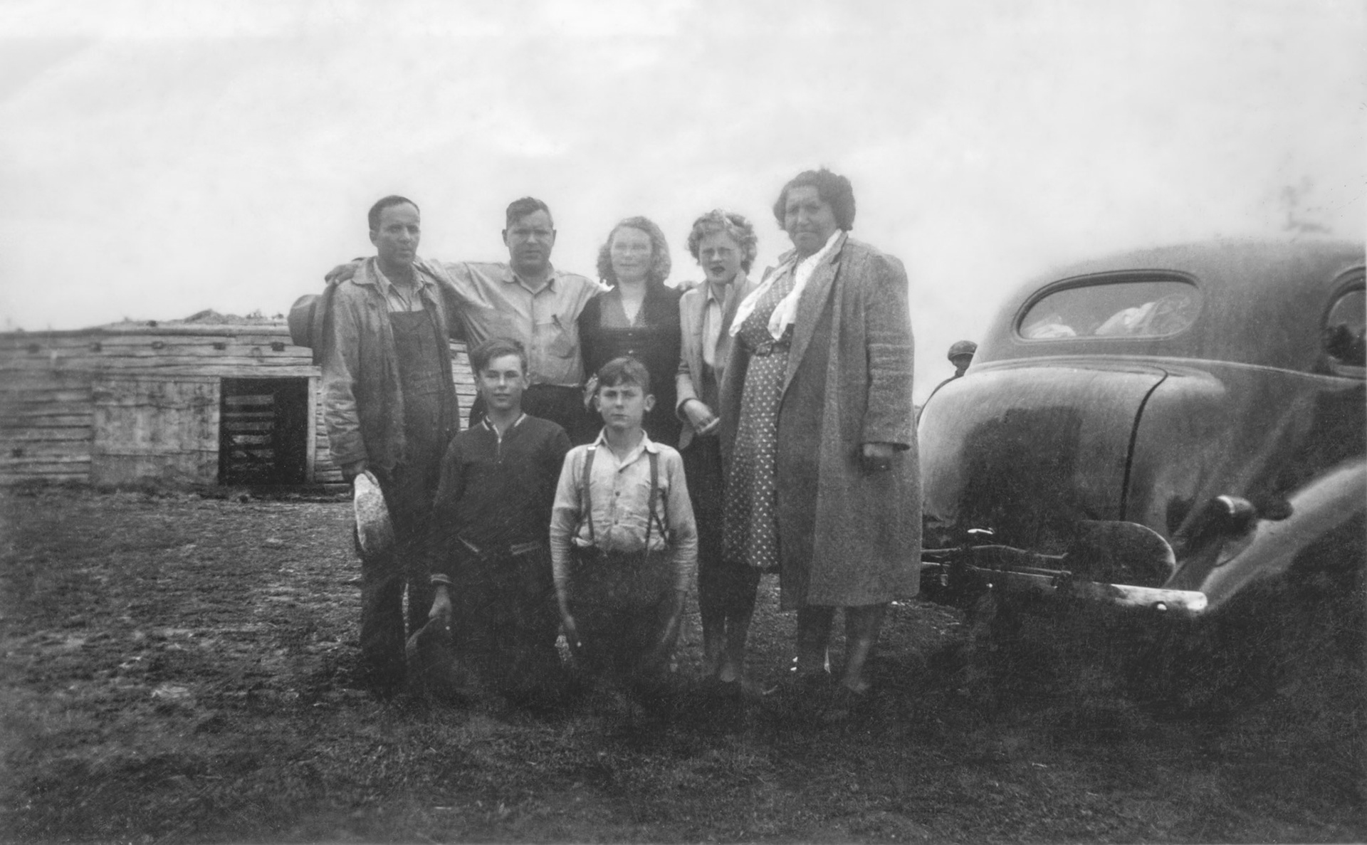 Circa 1945-48: Huculak brothers with family and spouses of parents Nykola (Nick) Huculak and Wasylna [Lena Yalischuk] Huculak (neither pictured). L to R: John Huculak SR -  brother Nick Shalk (Huculak) - Annie [Darda] Huculak (spouse of John) - Doris Huculak (daughter of Annie) - Alice Shalk (wife of Nick Shalk). Kneeling sons of John and Annie: George (Willis) and John Huculak JR. Taken on John and Annie family farm northwest of Willingdon, AB. Note male child peeking out behind car is same as reference in another photo taken same time. Photo restoration Brian M Huculak
