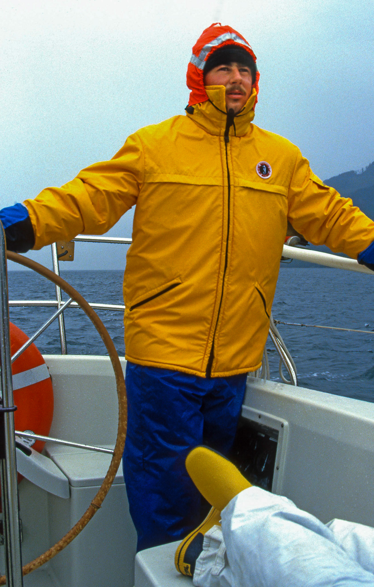 Circa 1995: Open water sailing, Pacific Ocean, west coast of Vancouver Island, British Columbis. Brian Huculak at the helm in some foul weather. Photo credit: Robert Keith.