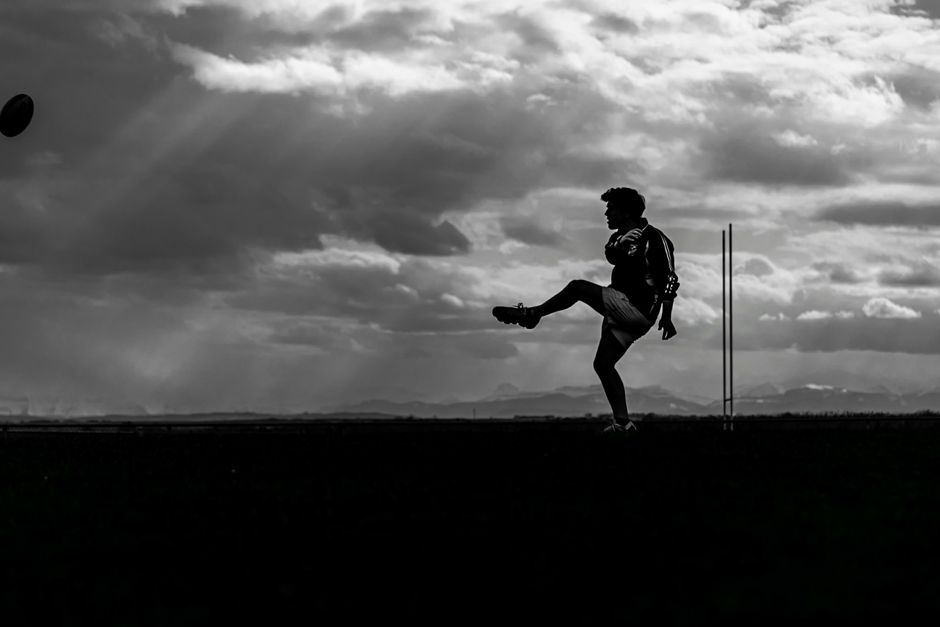 01 May 2018: Calgary Alberta. Garreth Emment (son of Lee-Ann [Huculak] Emment.) Stormy skies on the rugby pitch. I was attendding practice and liked the tension of the ball just staying in frame and the goal posts still in visible as Garreth boots one down pitch. Photo: Brian M Huculak