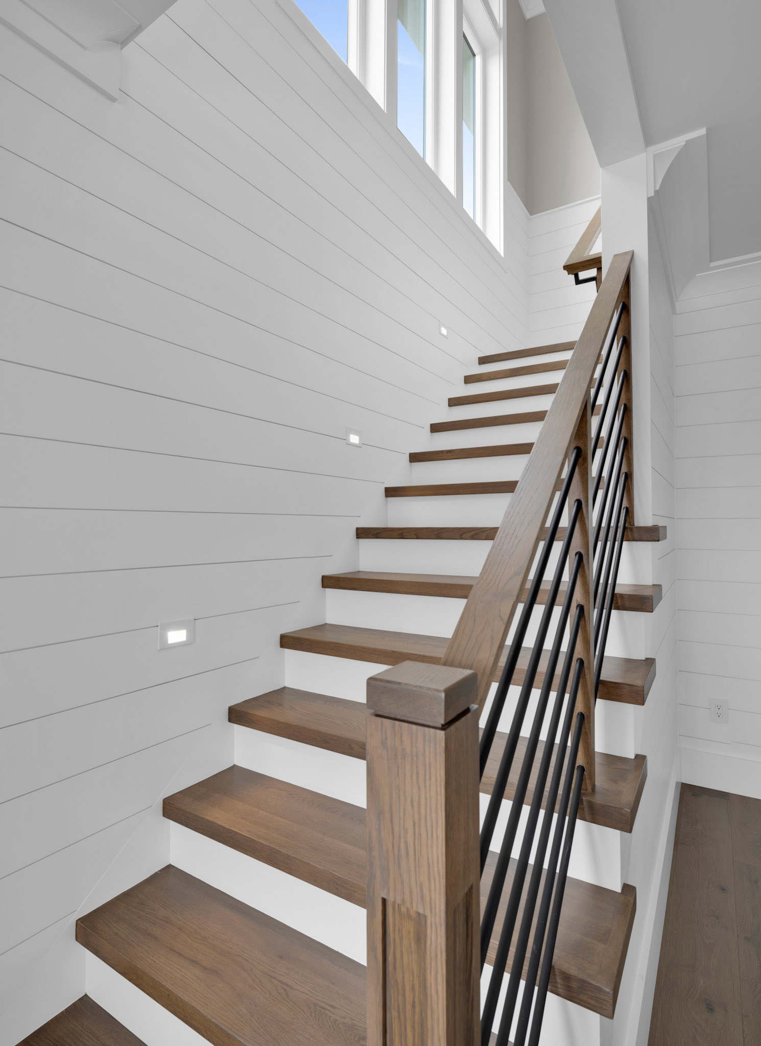 Open staircase with white shiplap walls, natural hardwood treads, and contemporary cable railings designed for modern waterfront living.