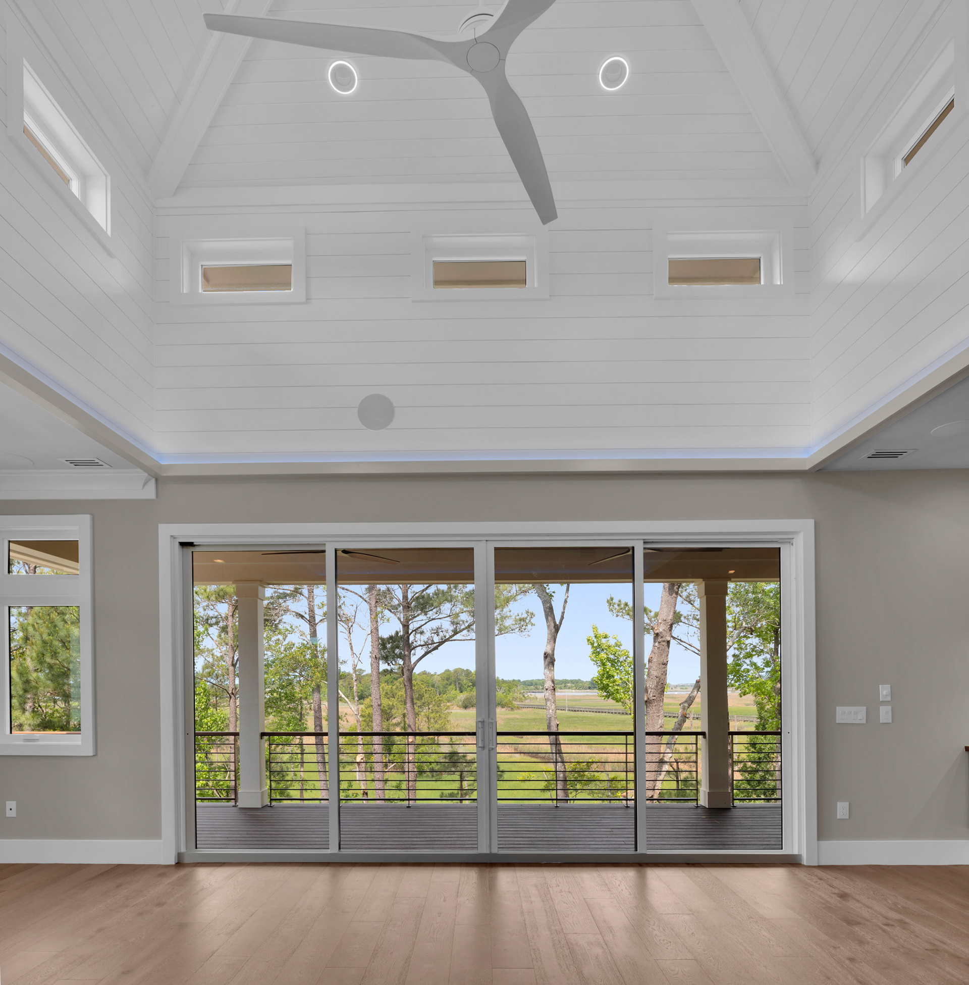 Bright waterfront great room featuring oversized panoramic doors, recessed lighting, and seamless indoor-outdoor living designed for modern coastal lifestyles.