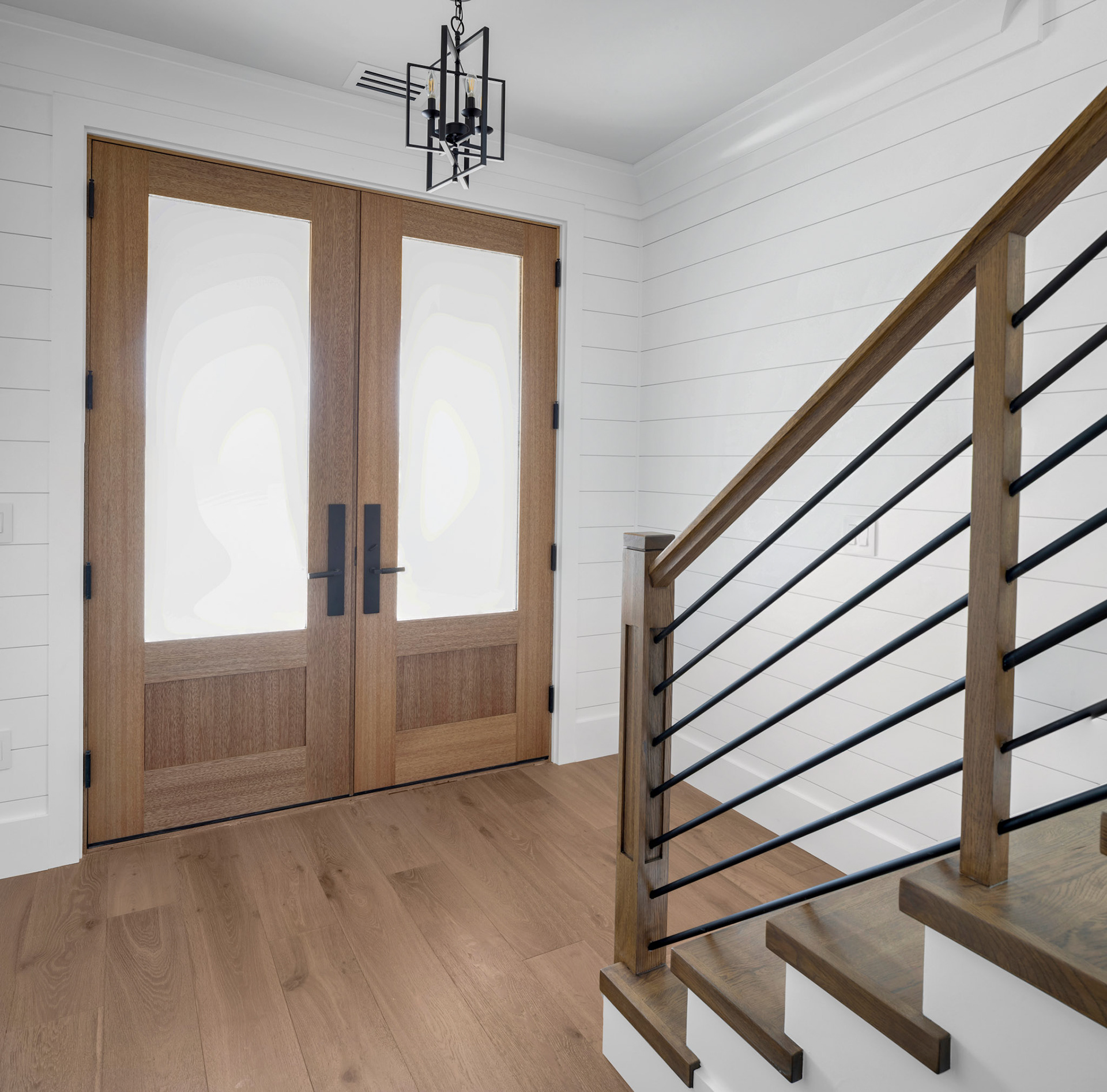 Modern coastal entryway with custom wood double doors, horizontal cable railing staircase, and bright shiplap wall detailing throughout the foyer.