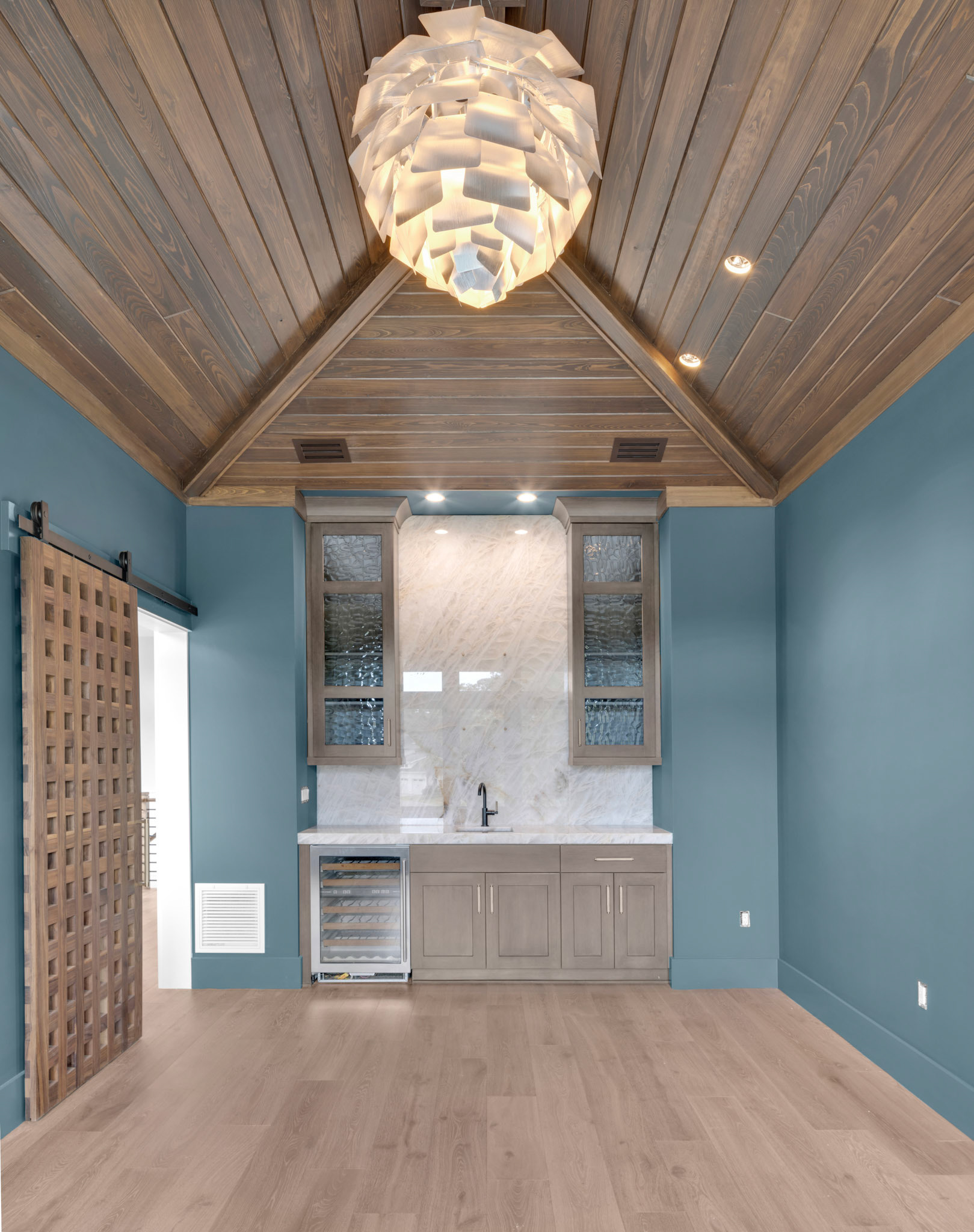 Elegant wine lounge featuring rich blue accent walls, custom cabinetry, designer chandelier, and warm natural wood ceiling finishes.