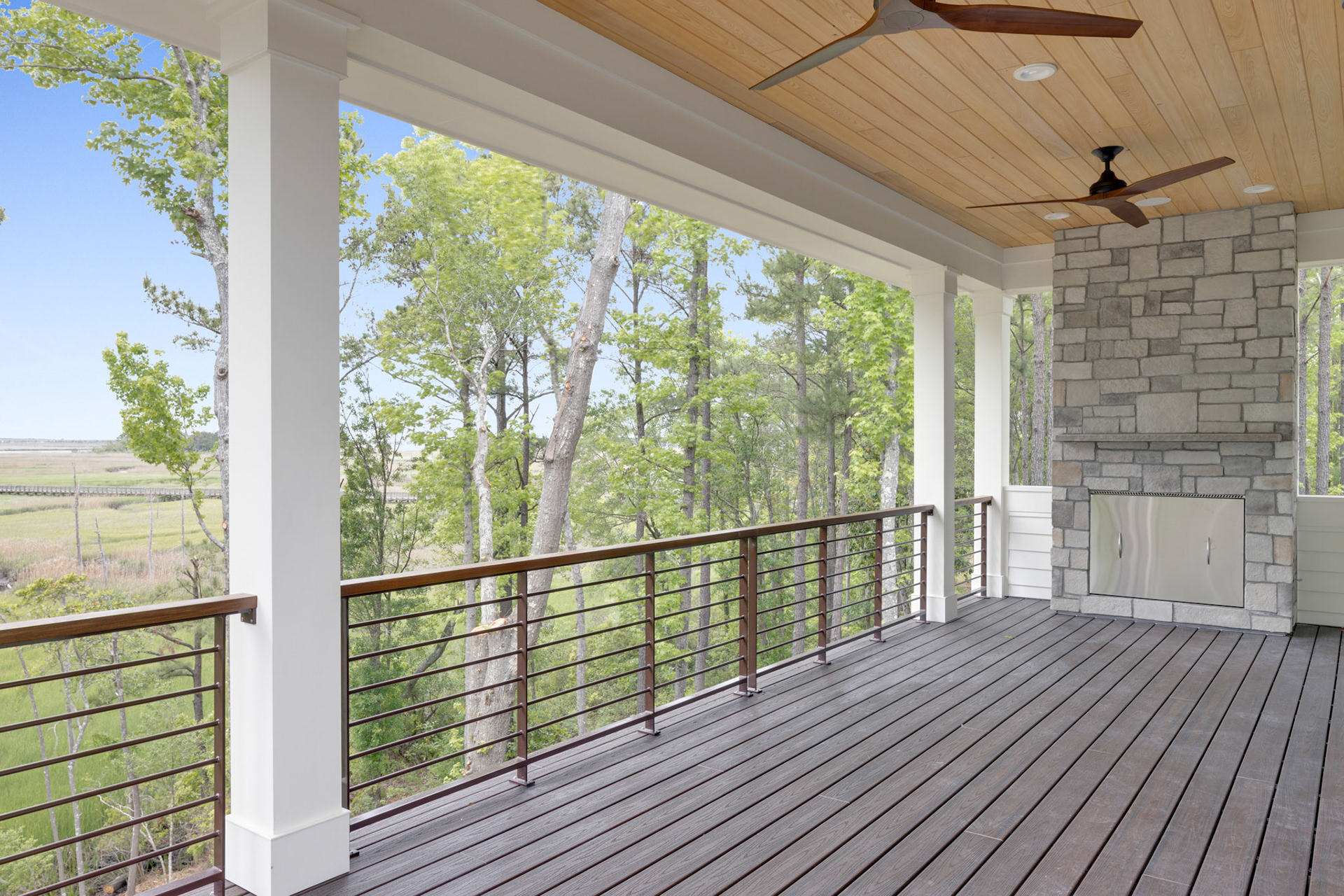 Covered outdoor living space with composite decking, tongue-and-groove wood ceiling, stone fireplace, and panoramic river views in coastal North Carolina.