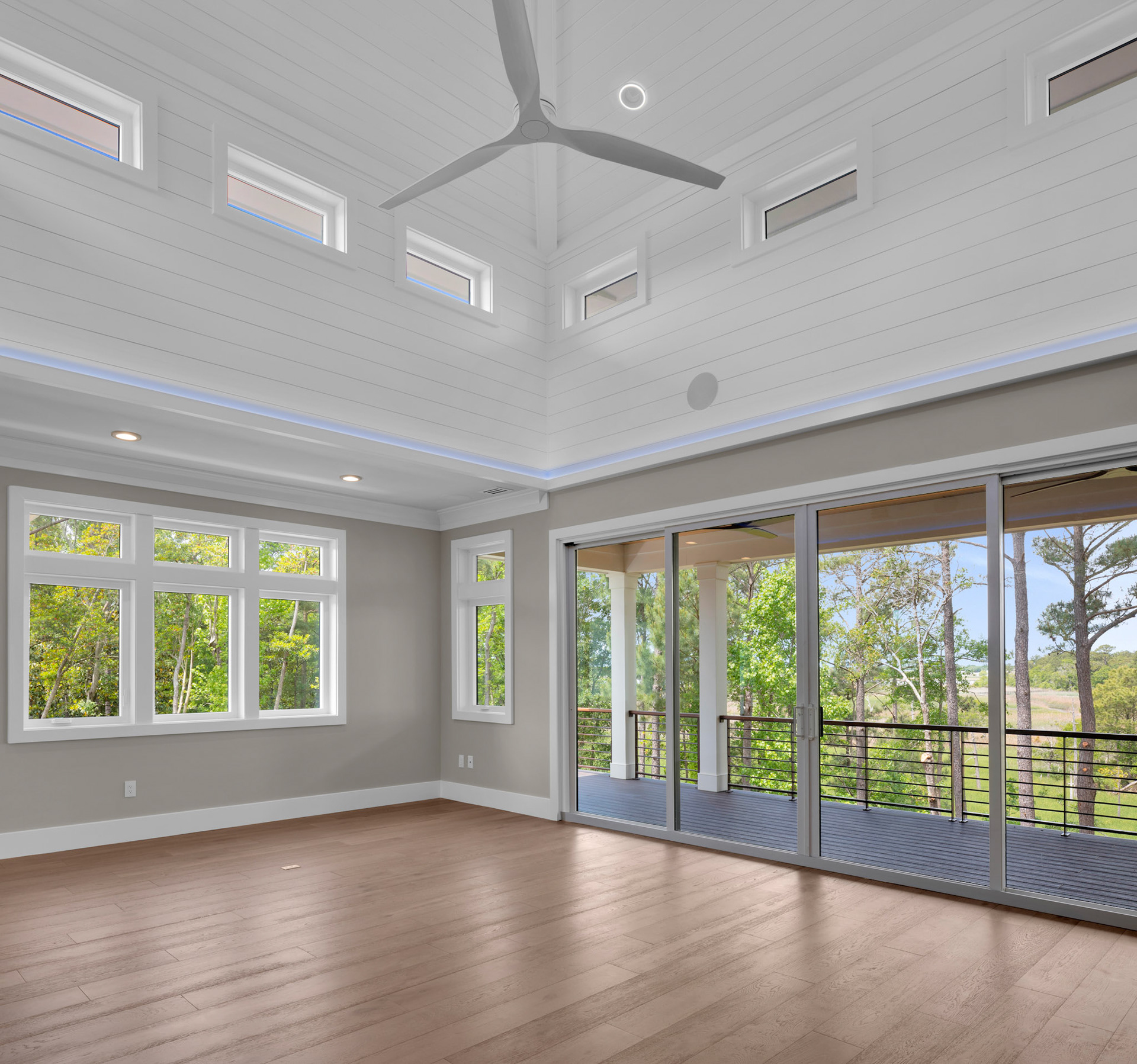 Open-concept coastal living room with vaulted shiplap ceilings, clerestory windows, and expansive sliding glass doors overlooking the river.