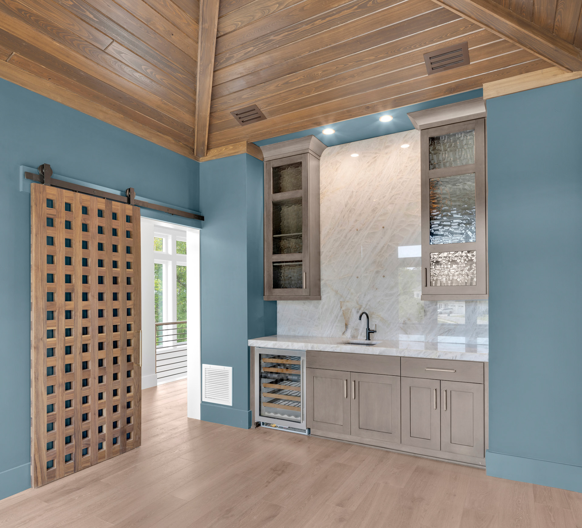 Custom wine room entrance with decorative wood lattice accents, vaulted tongue-and-groove ceiling, and built-in beverage storage.