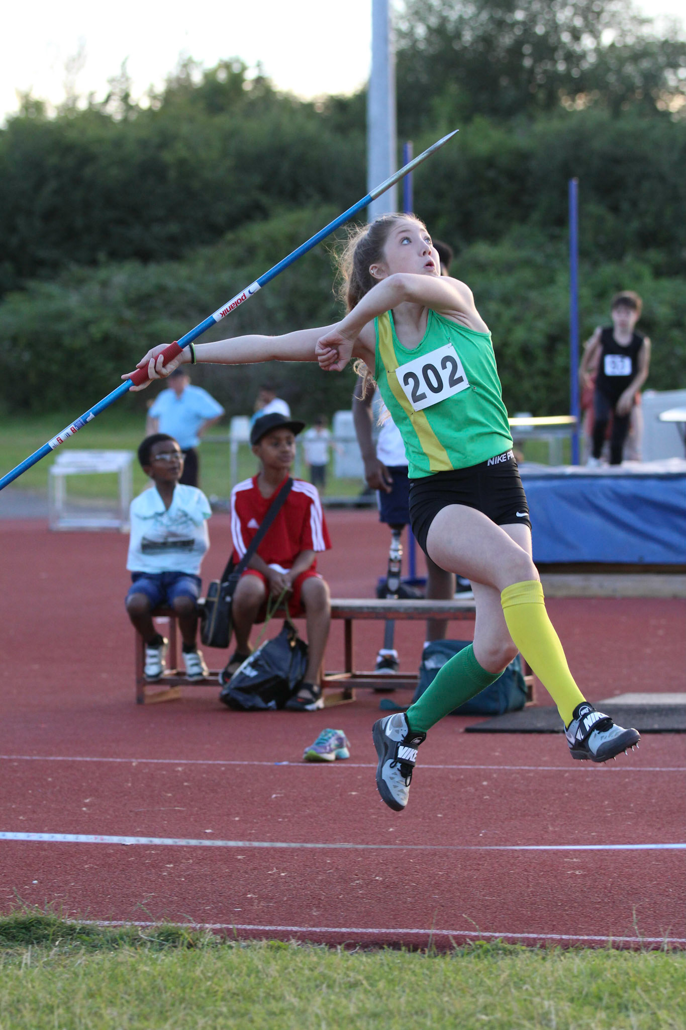 Two boys watch javelin at Summer evening athletics meet
