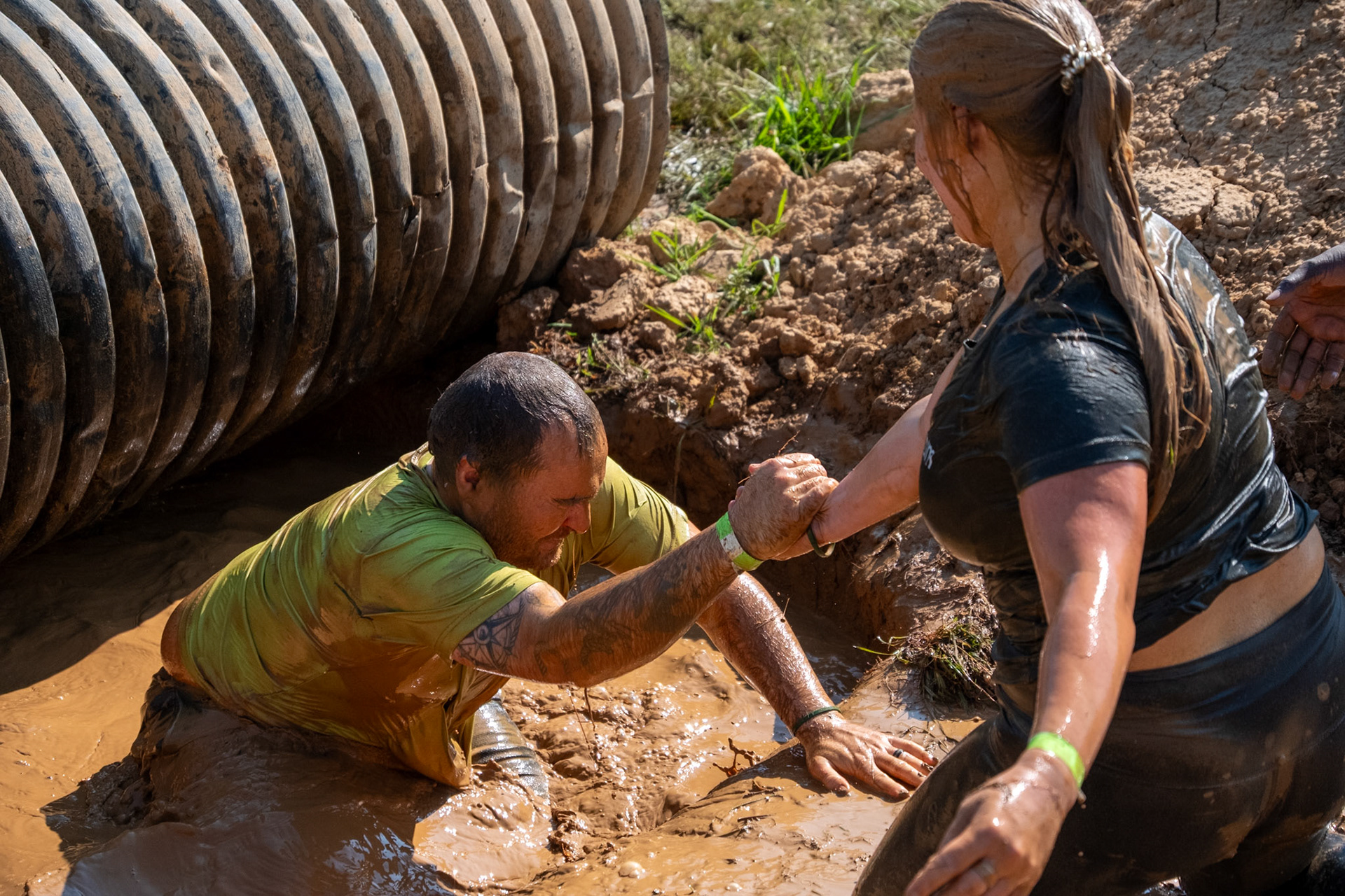 Participants of the annual Bowling Green Mud Run assist one another after swimming under an obstacle at Phil Moore Park on Aug. 23.