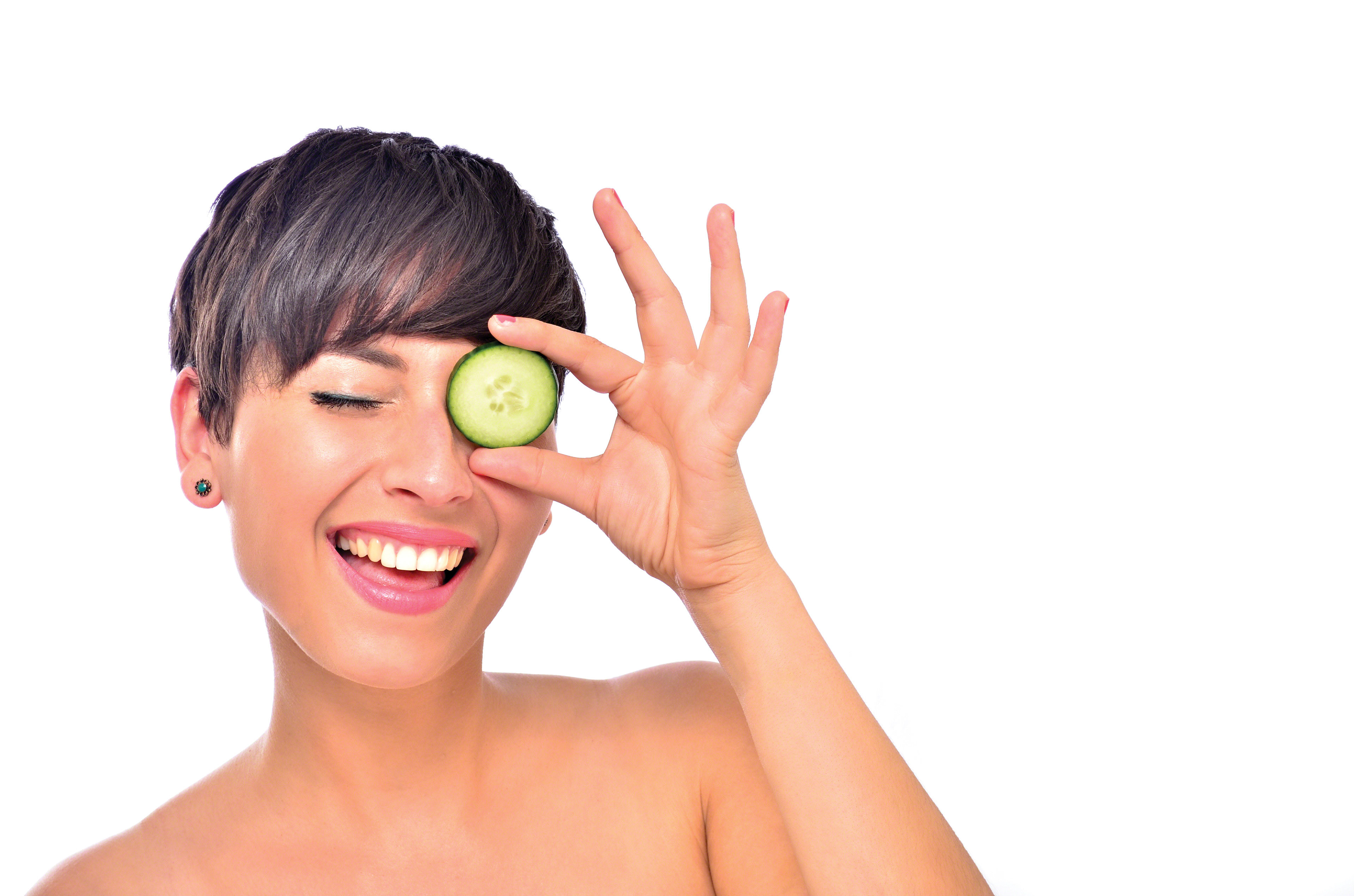 Studio image of Brunette Female model winking and holding a slice of cucumber over her eye