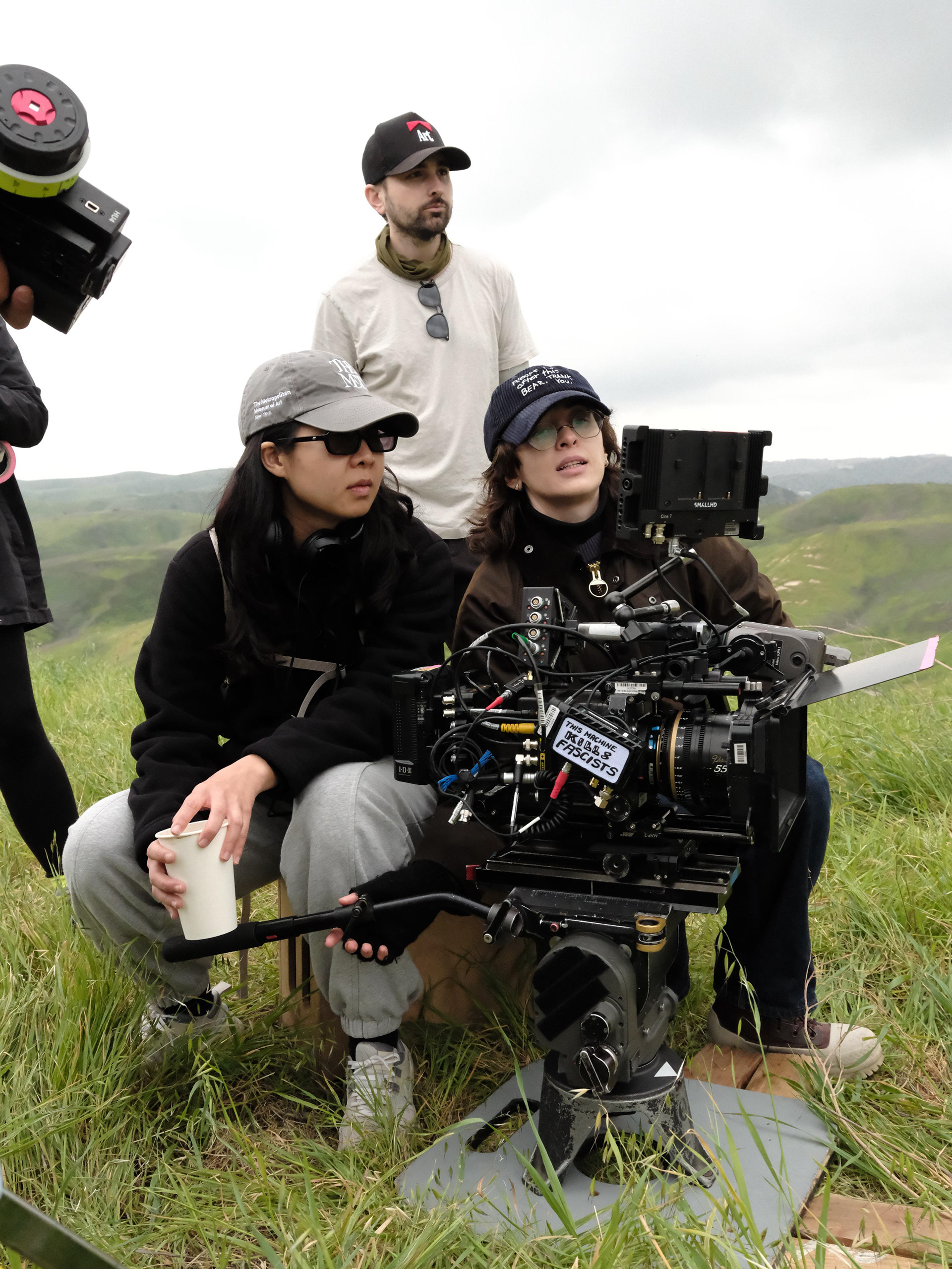 Production designer Austyn James standing behind the camera crew on an outdoor film set.