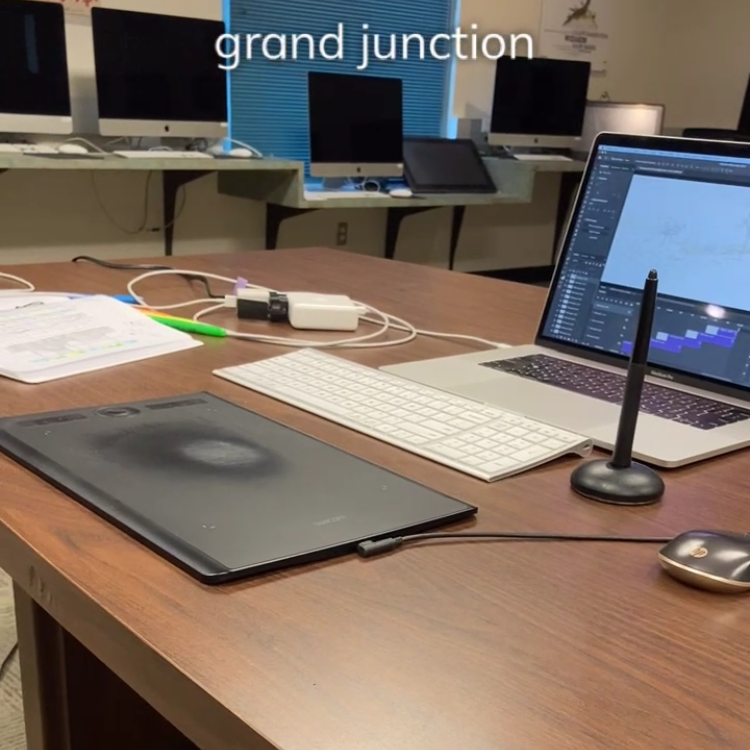 A Wacom Intuos drawing tablet, macbook laptop, notebook, and other tools on a table in a computer lab
