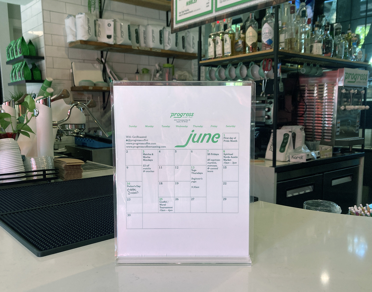 The calendar, printed on US Letter size paper in a display holder on the counter of a coffee shop.
