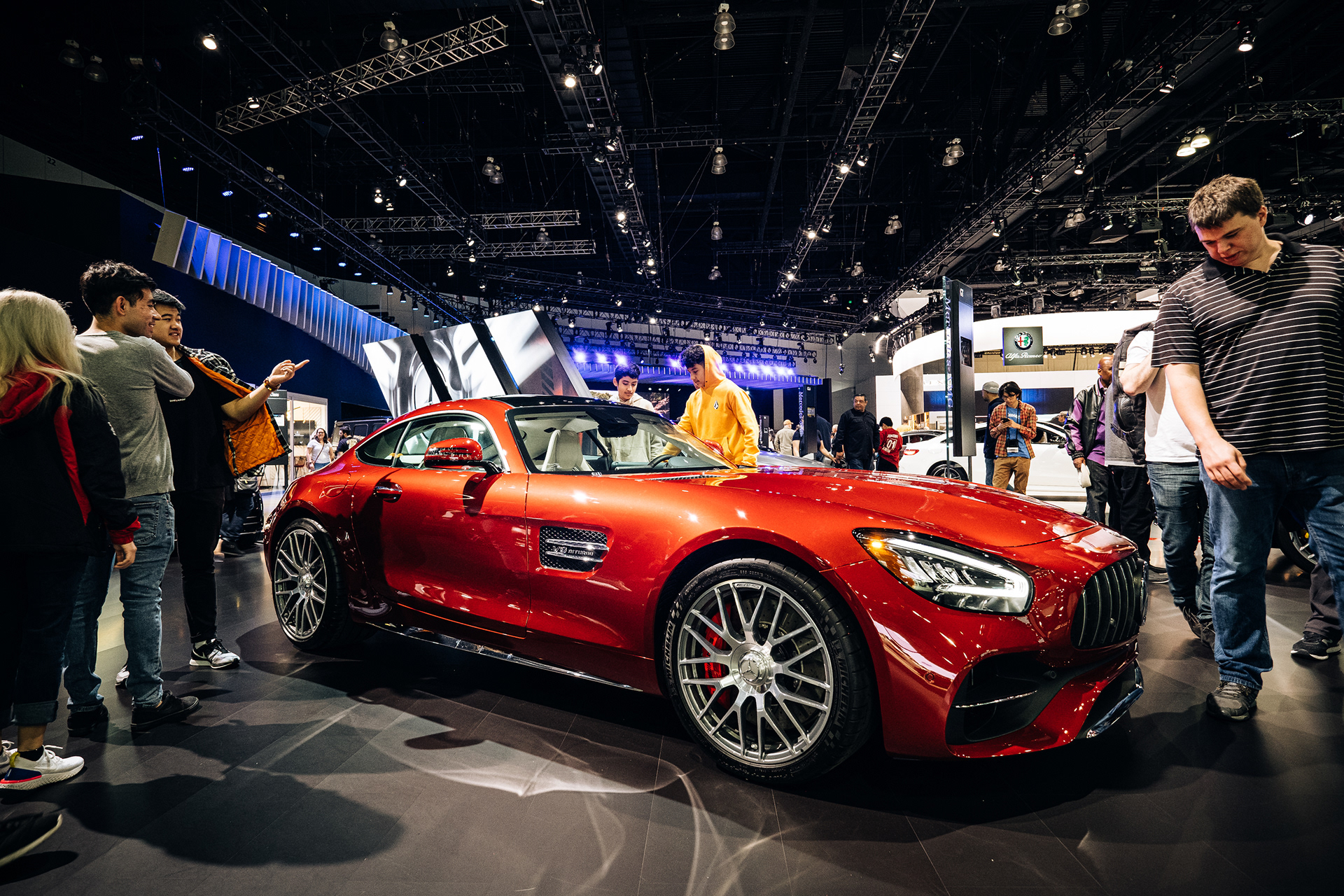 Visitors examining a red Mercedes-AMG sports car at an auto show.