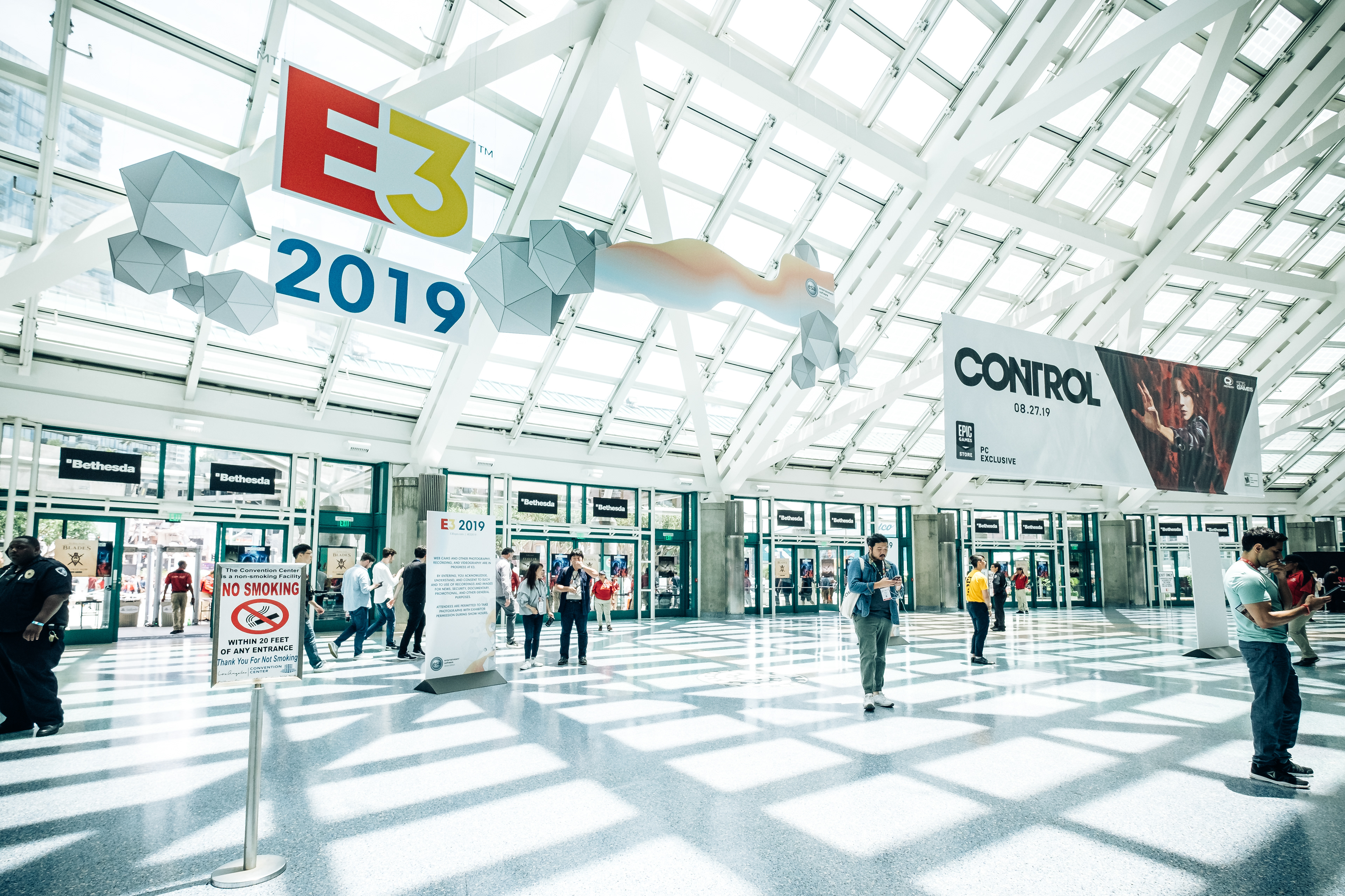 Attendees in the sunlit entrance hall beneath E3 2019 signs and exhibition banners.