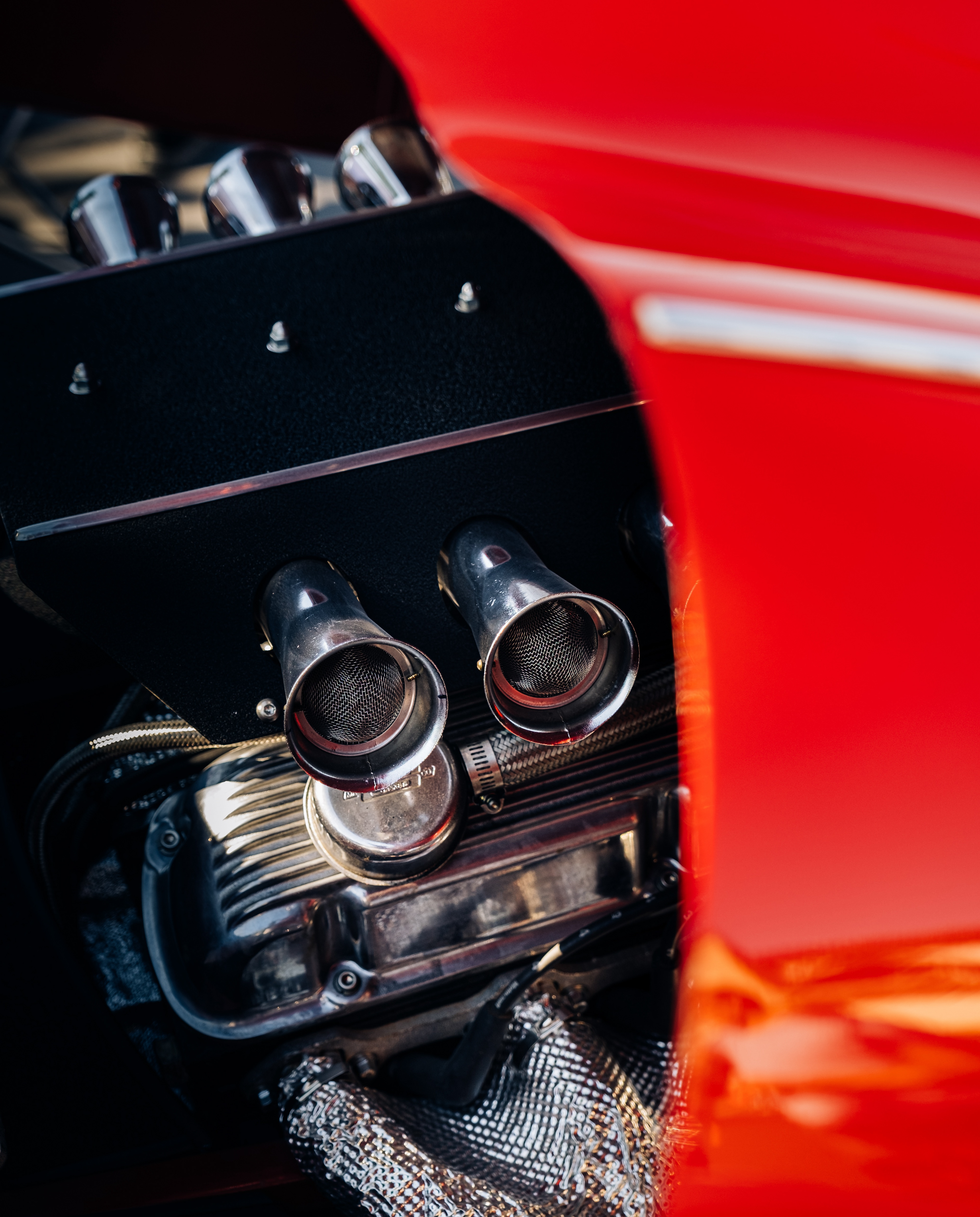 Close-up of polished engine intake trumpets framed by the red bodywork of a vintage car.