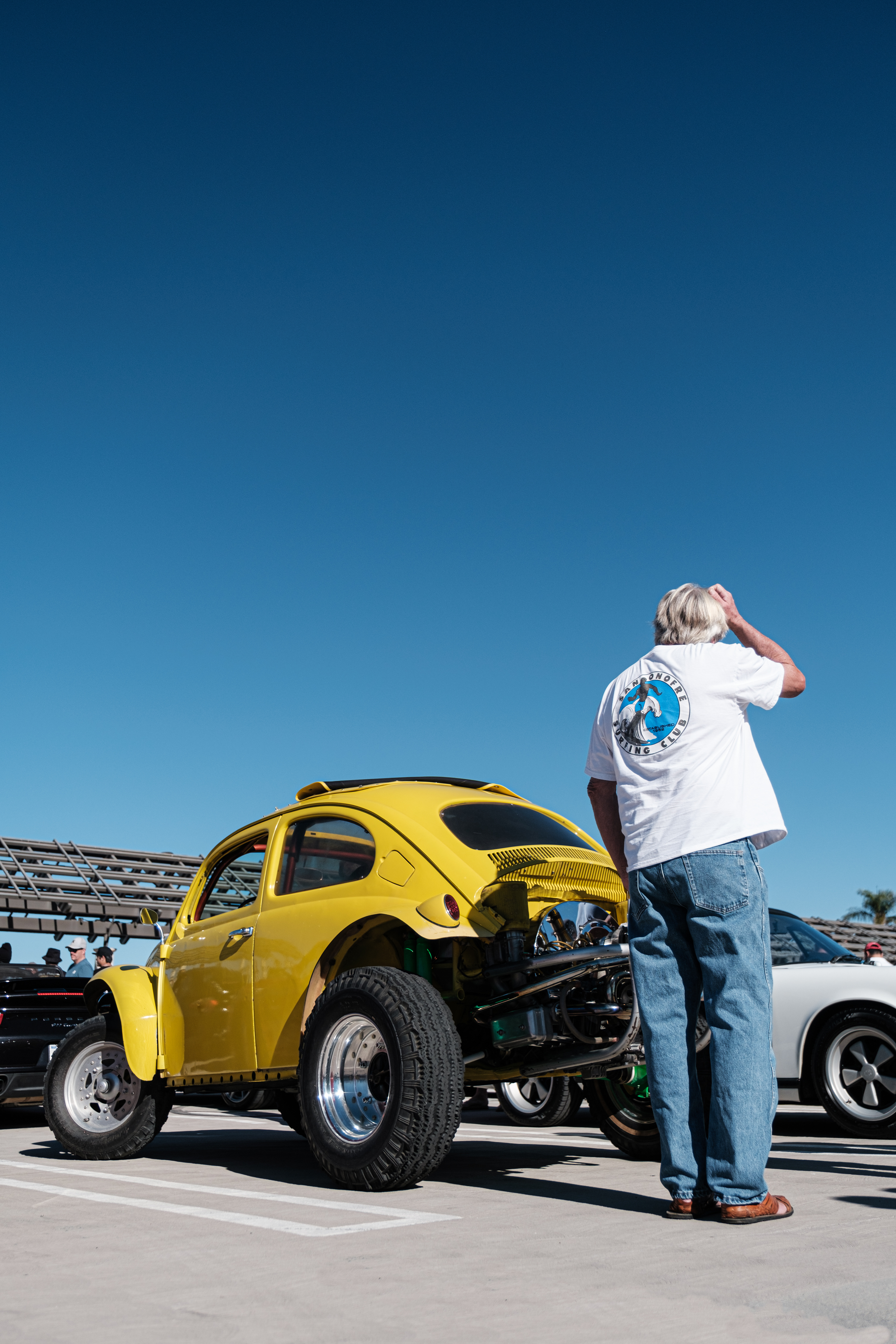 Visitor beside a yellow modified Volkswagen Beetle with an exposed rear engine at an outdoor car show.