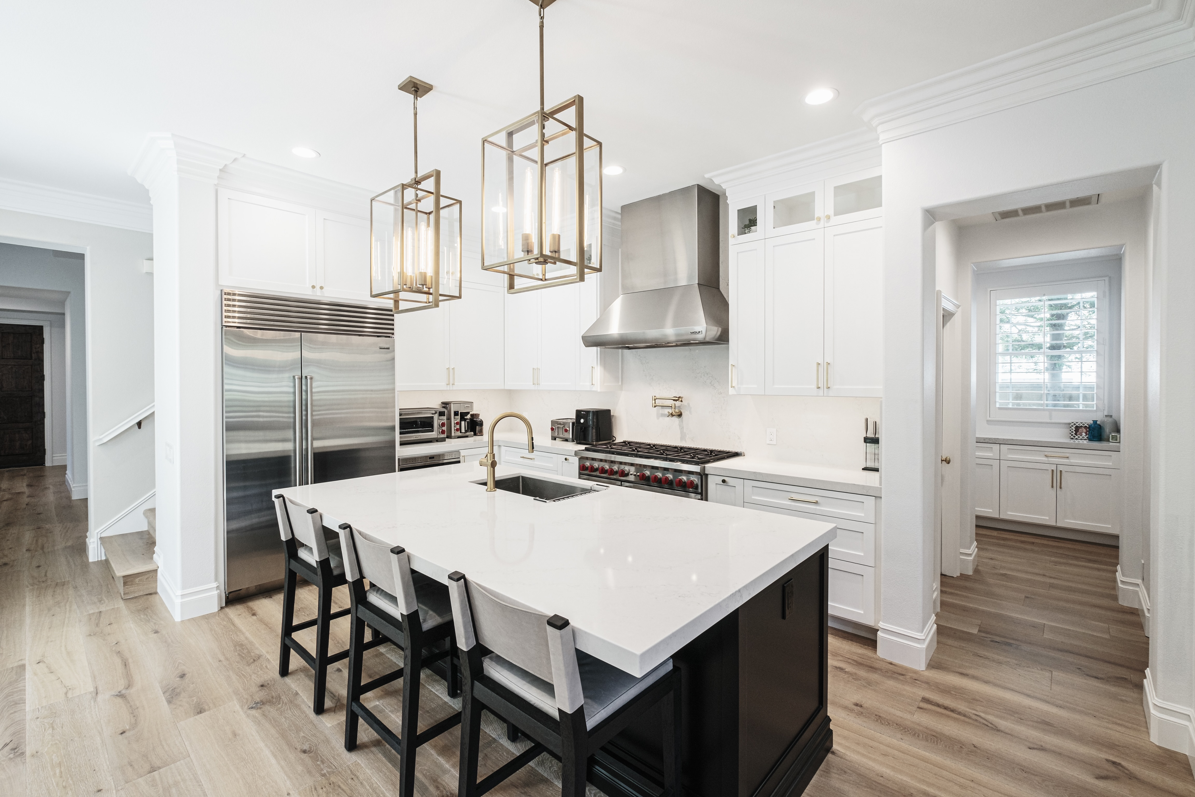 Remodeled kitchen in Coto de Caza, Orange County, with white cabinetry, a dark-base island, bar seating and brass-toned pendant lights.