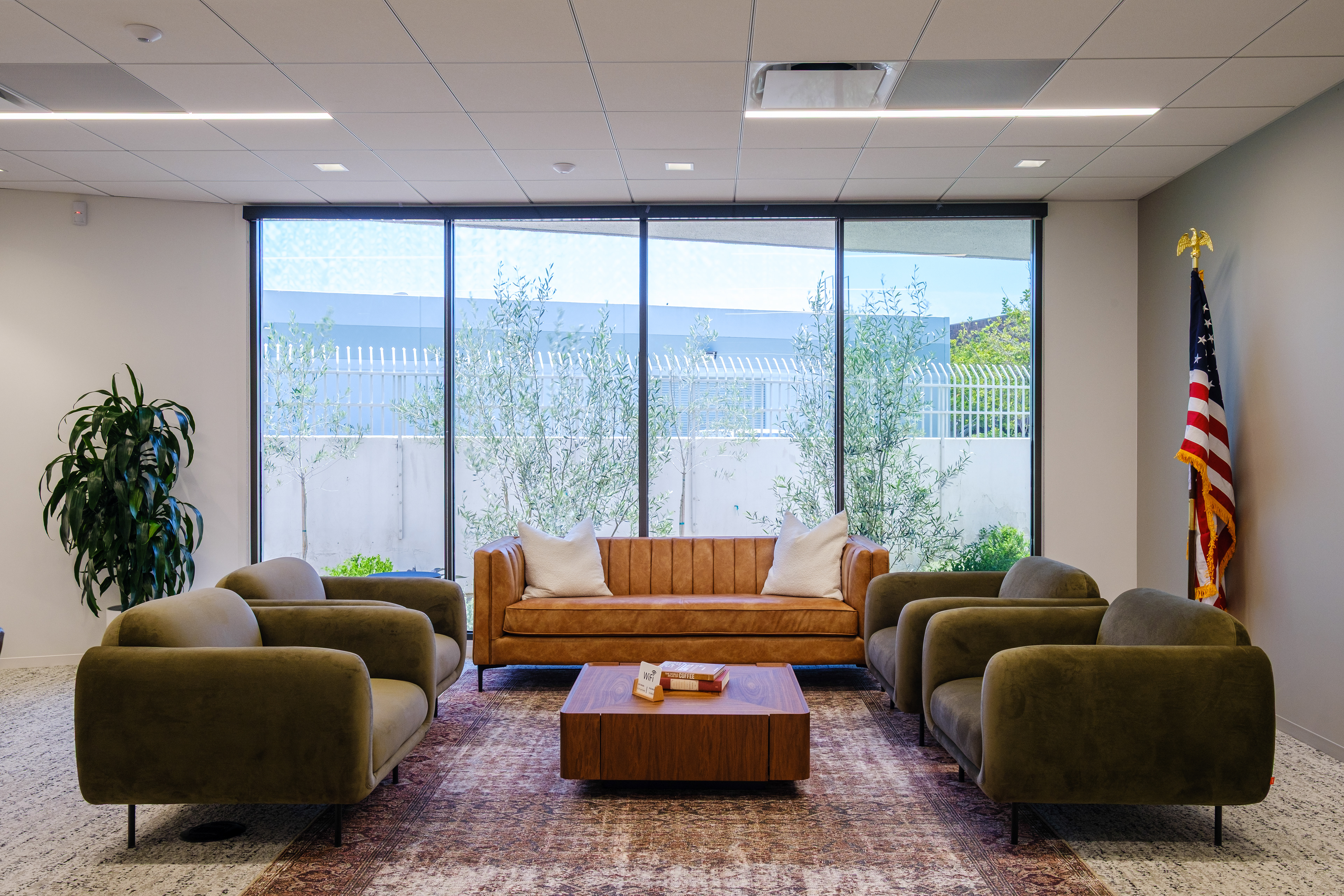 Office lounge with green armchairs, a tan sofa and large windows