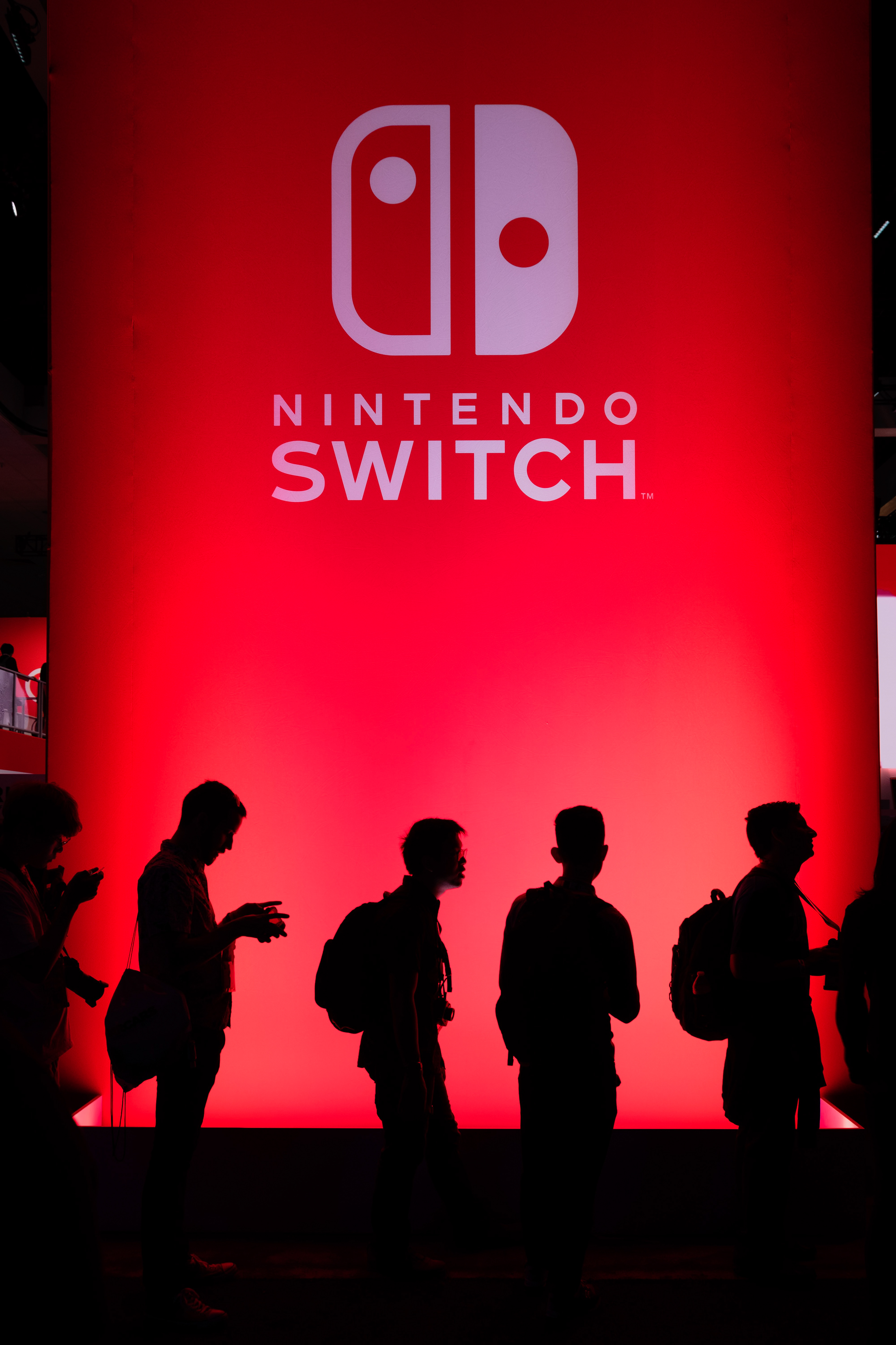 Silhouetted attendees beneath a red Nintendo Switch exhibition display.