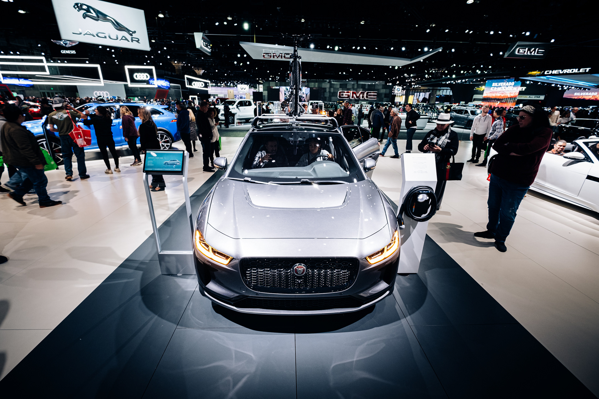 Silver Jaguar displayed among visitors at an indoor auto show.