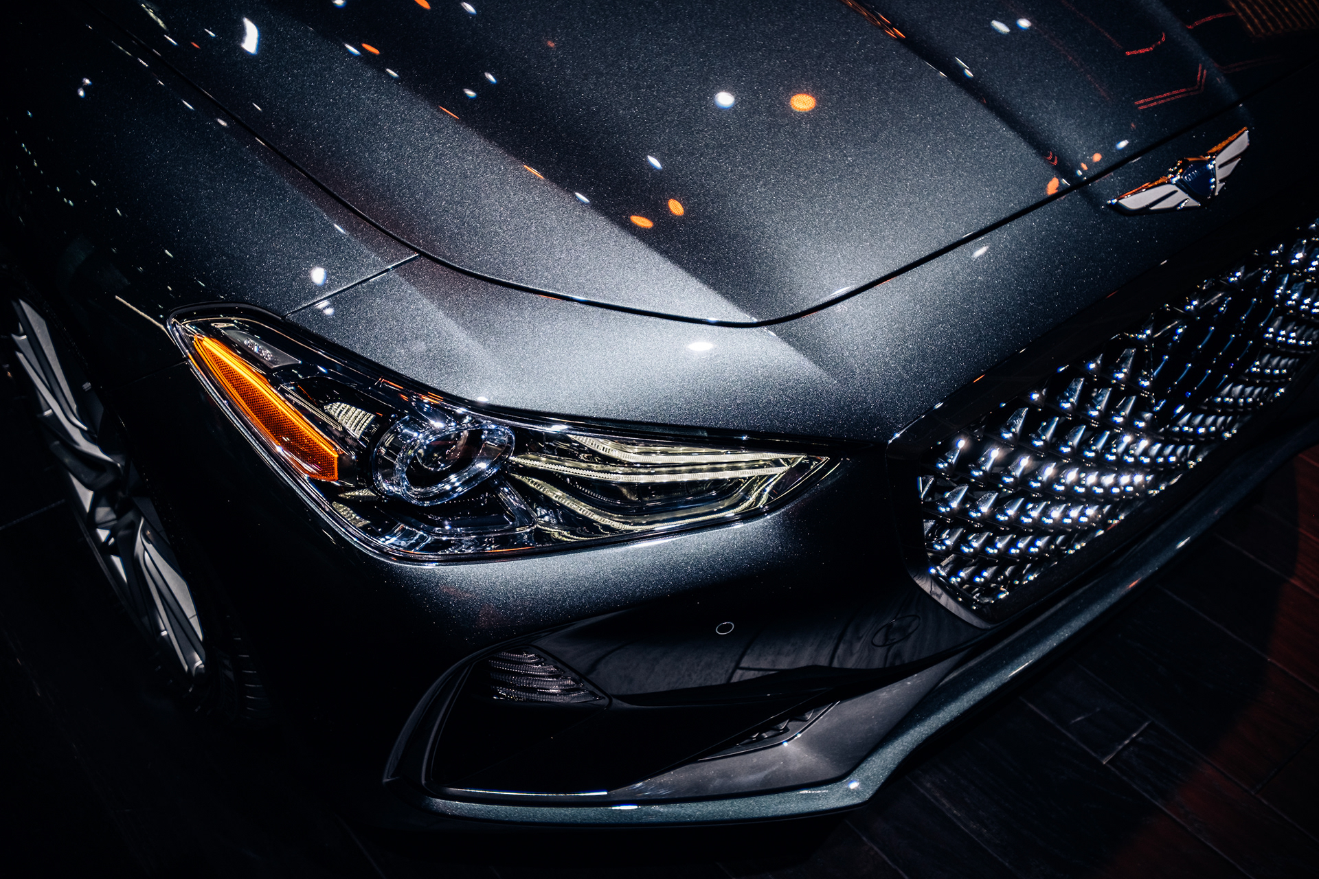 Close-up of a gray Genesis sedan’s headlight, sculpted hood and front grille.