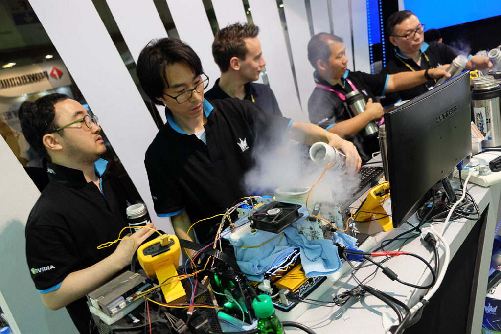 Computer hardware demonstration with presenters, monitors and visible cooling vapor.
