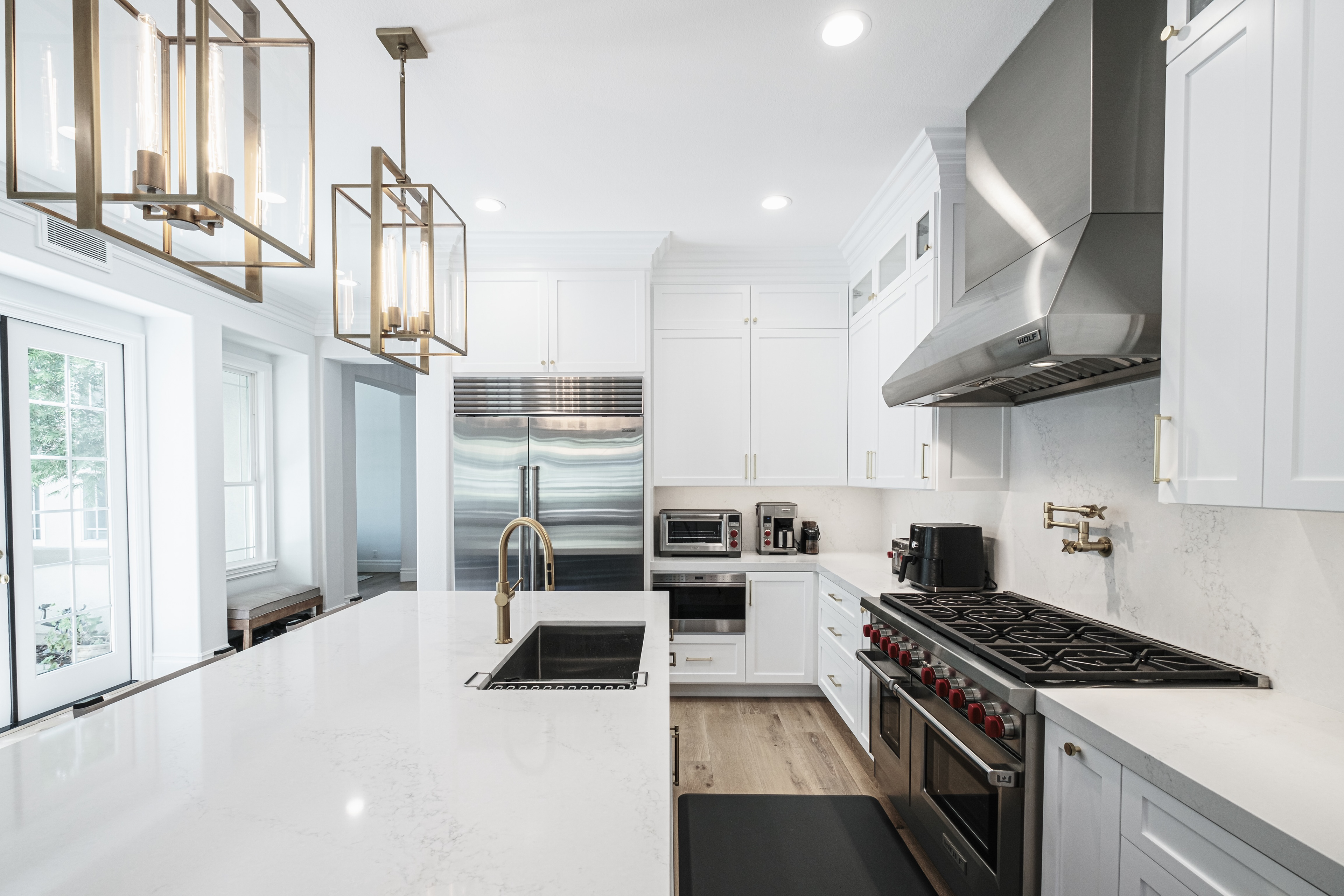 White kitchen showing an island sink, stainless steel range, refrigerator and pendant lights.