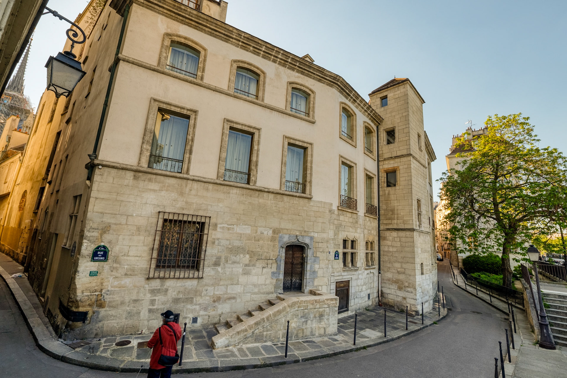 Stone upon stone, this quiet house gathers the hushed prayers and forgotten songs of centuries past. Heavy wooden doors guard secrets of choir singers who once walked these winding lanes, their voices rising to the cathedral spire still visible above. In the golden morning light, Rue des Chantres feels suspended between worlds – where medieval shadows linger silently amidst the pulse of modern Paris