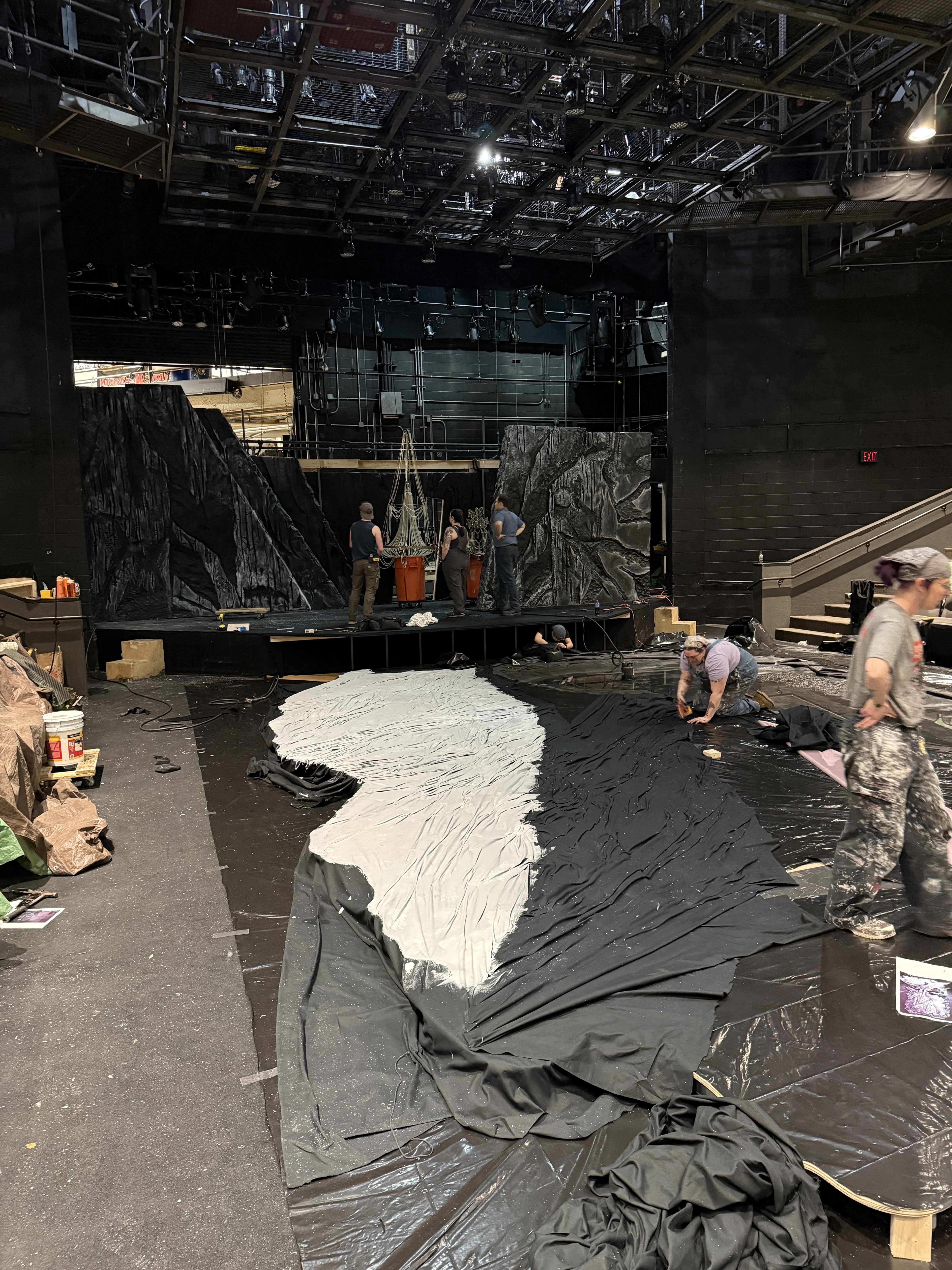 Scenic charge Diane stapling fabric for the slate deck while the carpentry team works to deadhang a chandelier
