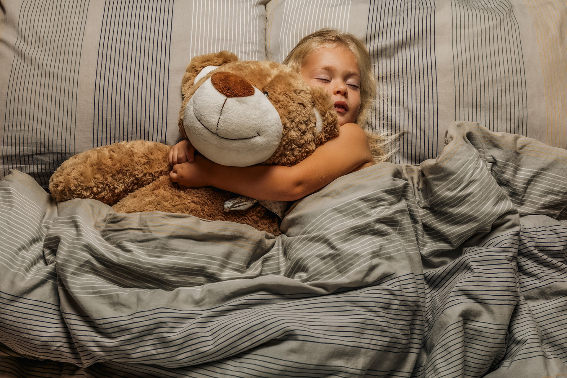 Enfant profondément endormi serrant son doudou contre lui. Illustration d’un sommeil réparateur et de l’accompagnement des difficultés de sommeil par la sophrologie.