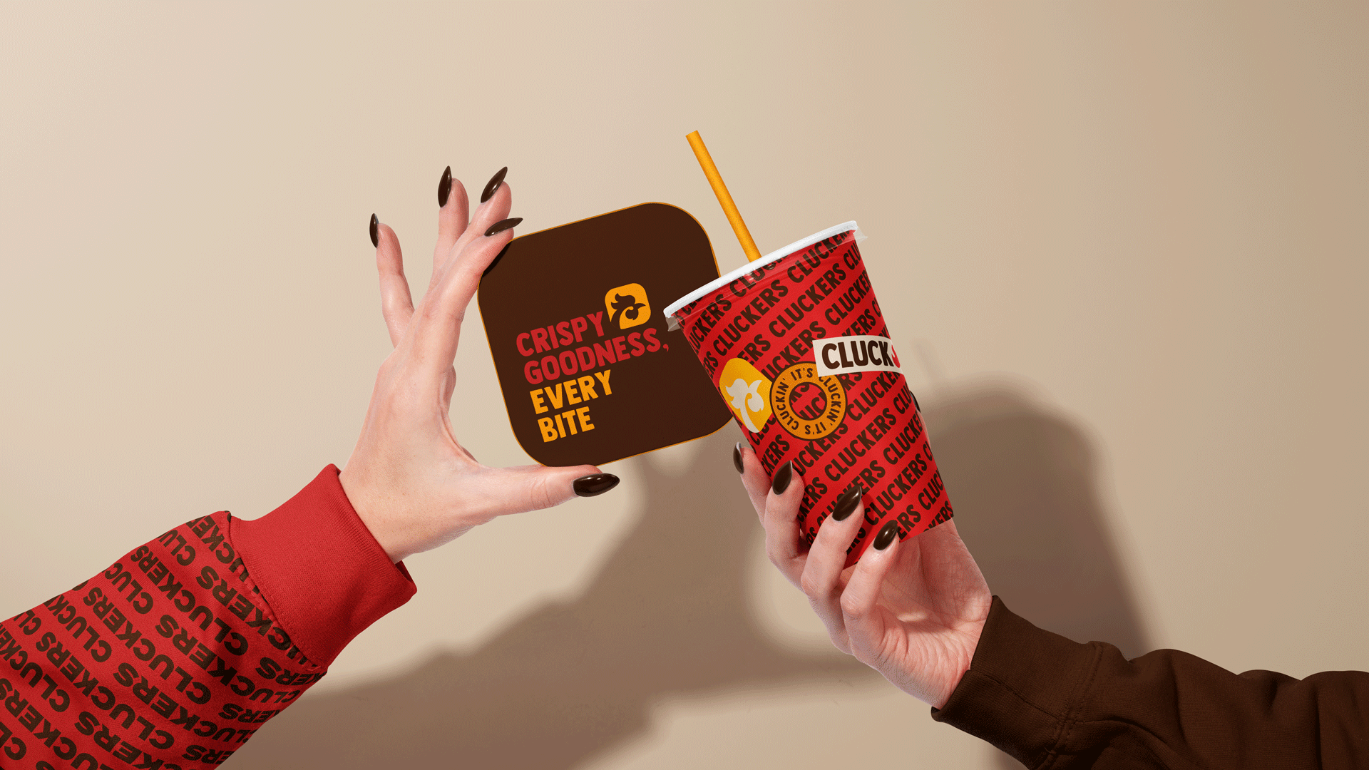 Hand holding a vibrant red Cluckers takeaway cup with a yellow straw against a beige background. The cup features a repeating CLUCKERS wordmark pattern, a custom C logo mark, an "It's Cluckin'" circular badge, and a CLUCK sticker. Fast food branding and packaging design by INDUSTRIA® Branding Co.