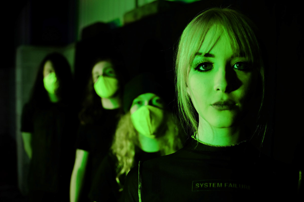Four DACARA band members stood in a line with green lighting. Vocalist Emma Shippen at the front