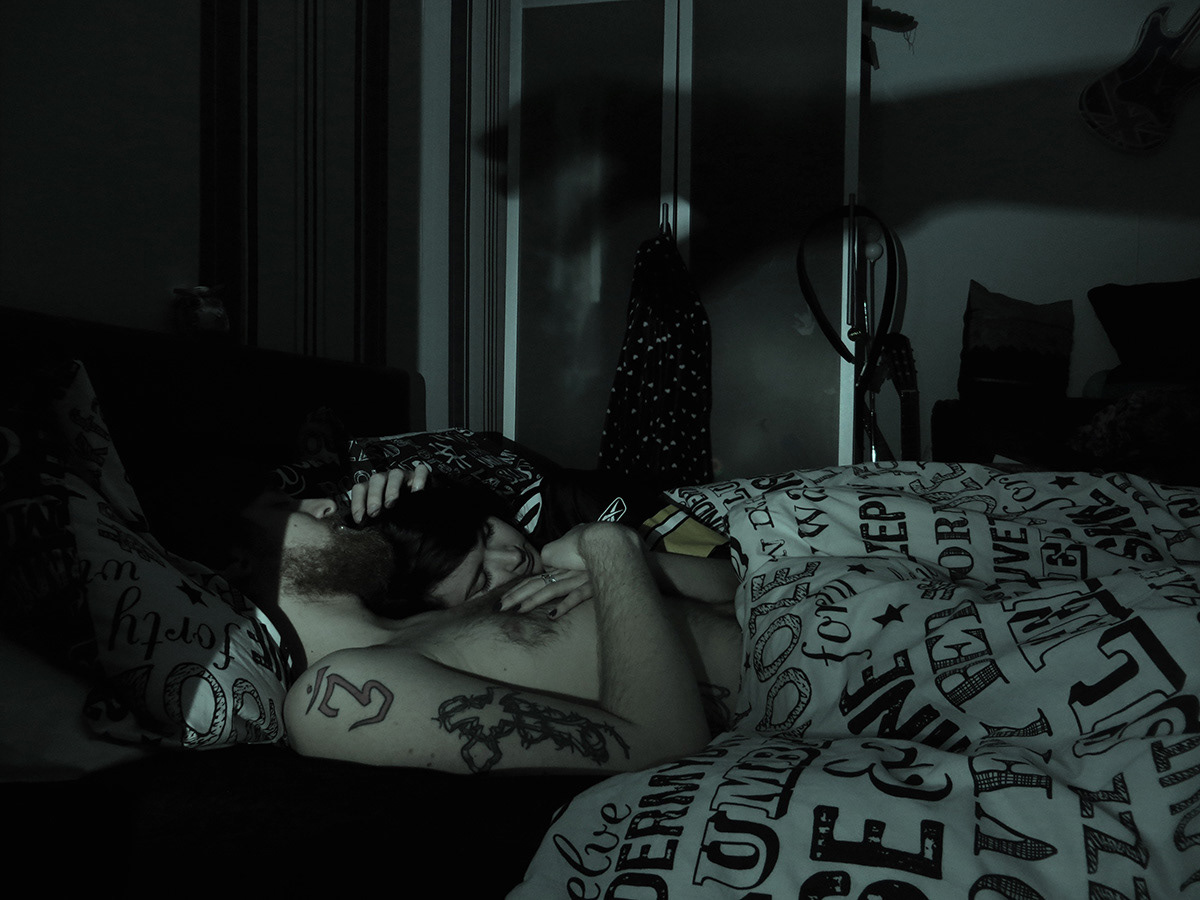 Dark photo with green hues of couple sleep in bed with the shadow of a hand reaching over them