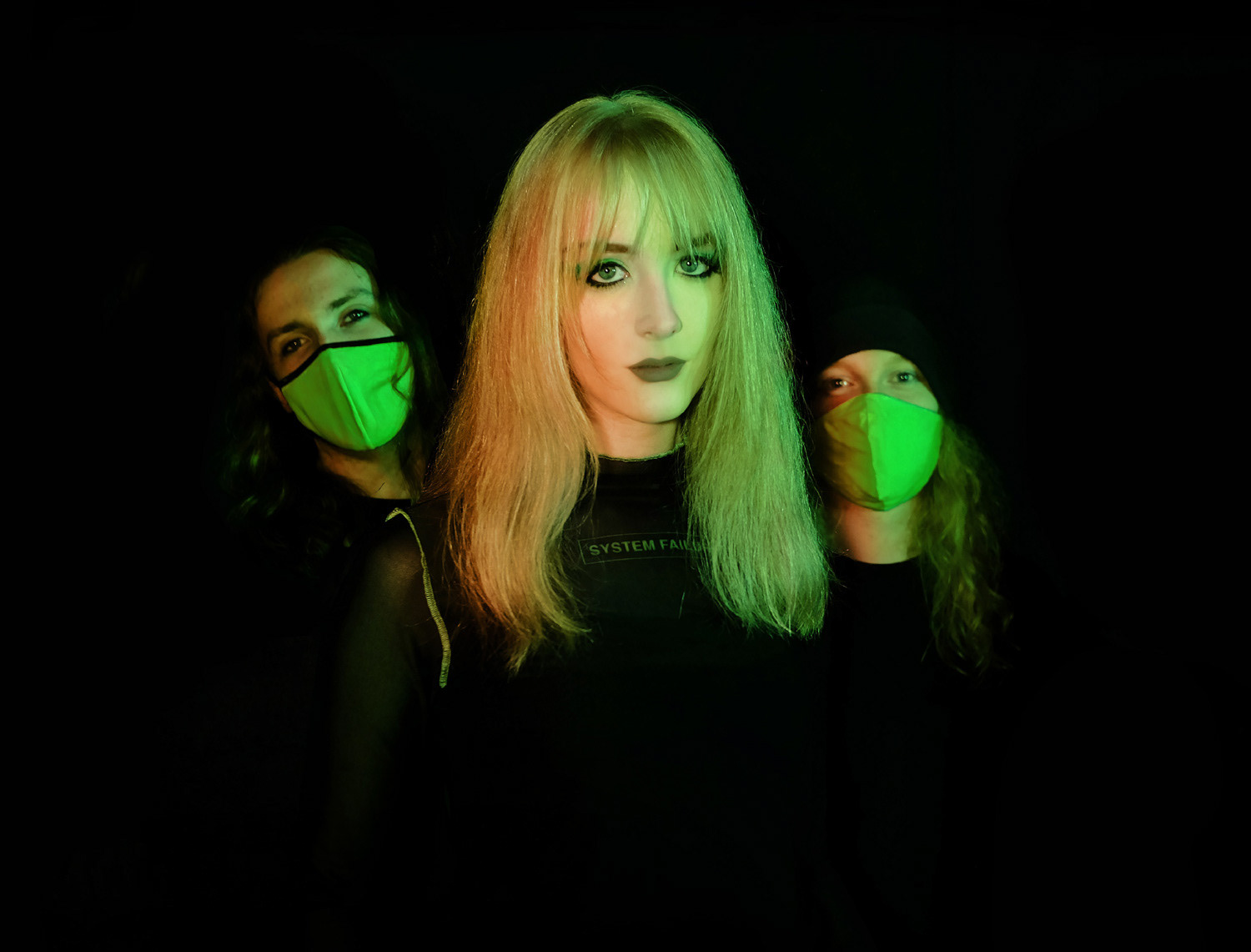 Three DACARA band members with green and orange lighting, looking at camera