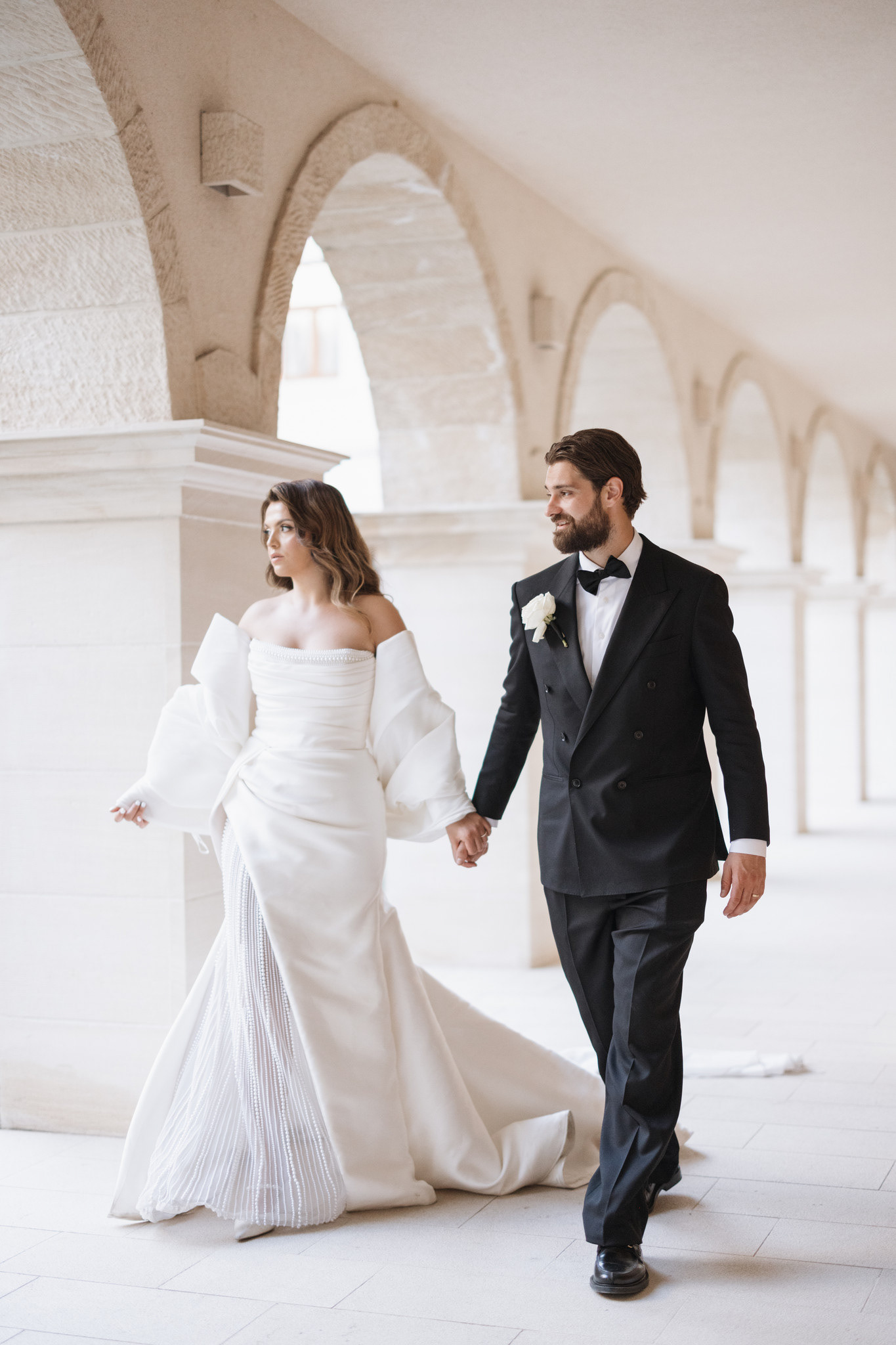 Bride and groom holding hands while walking through stone arches on their wedding day