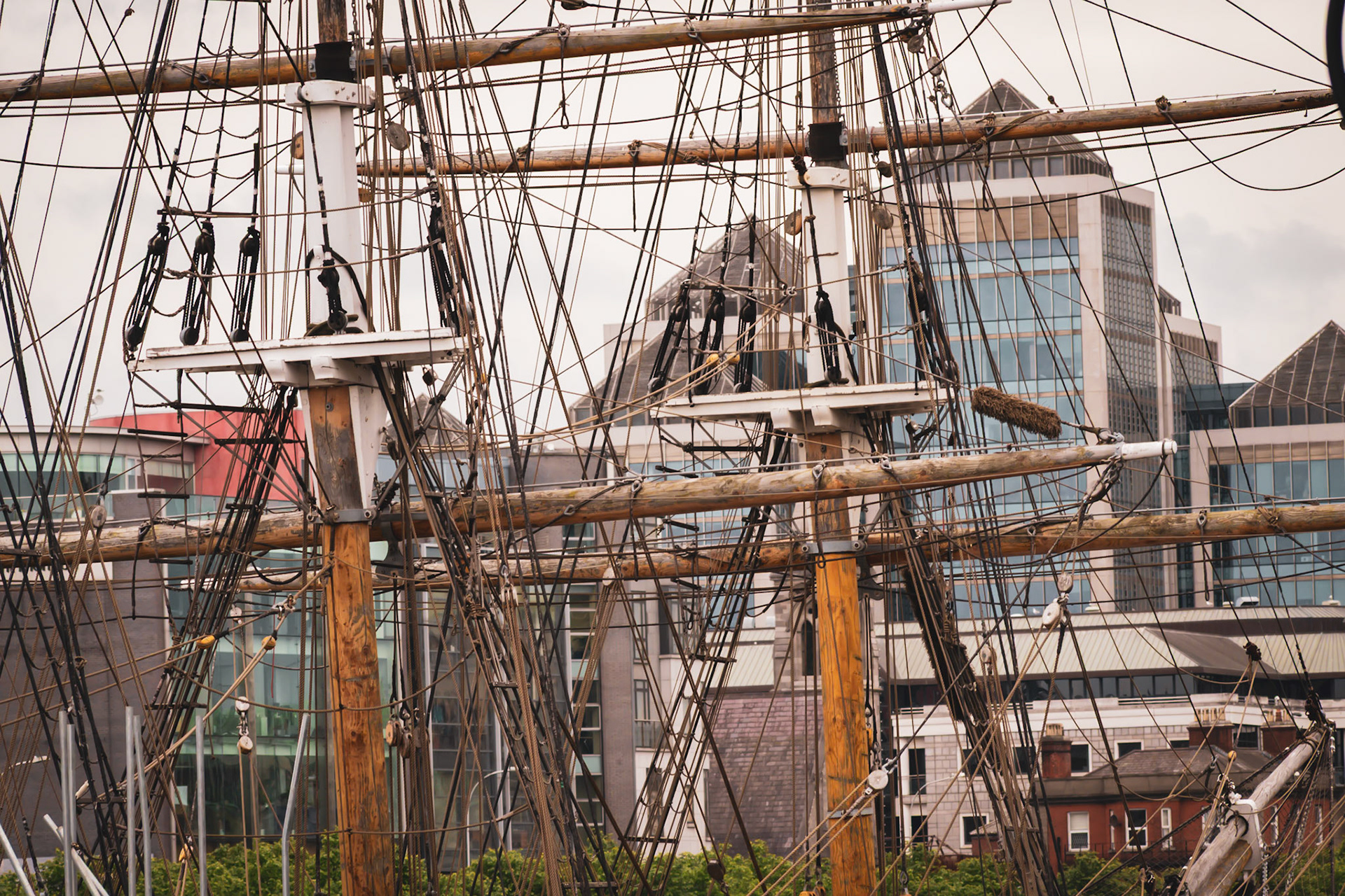A visual look at Dublin’s maritime history, where the wooden masts and rigging of a famine ship replica stand against the modern city skyline.