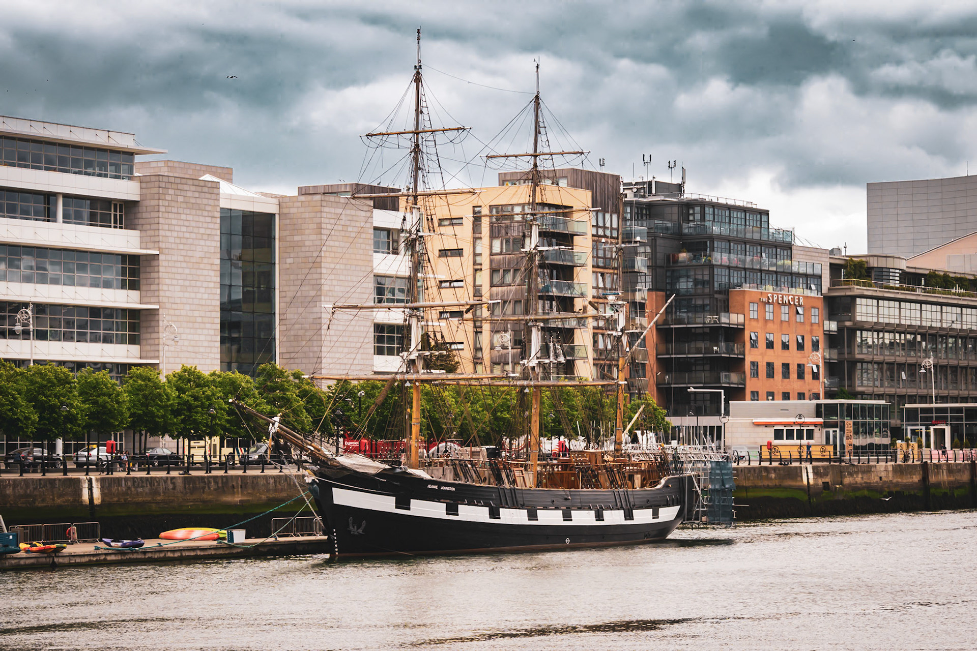 A visual look at Dublin’s maritime history, where the wooden masts and rigging of a famine ship replica stand against the modern city skyline.