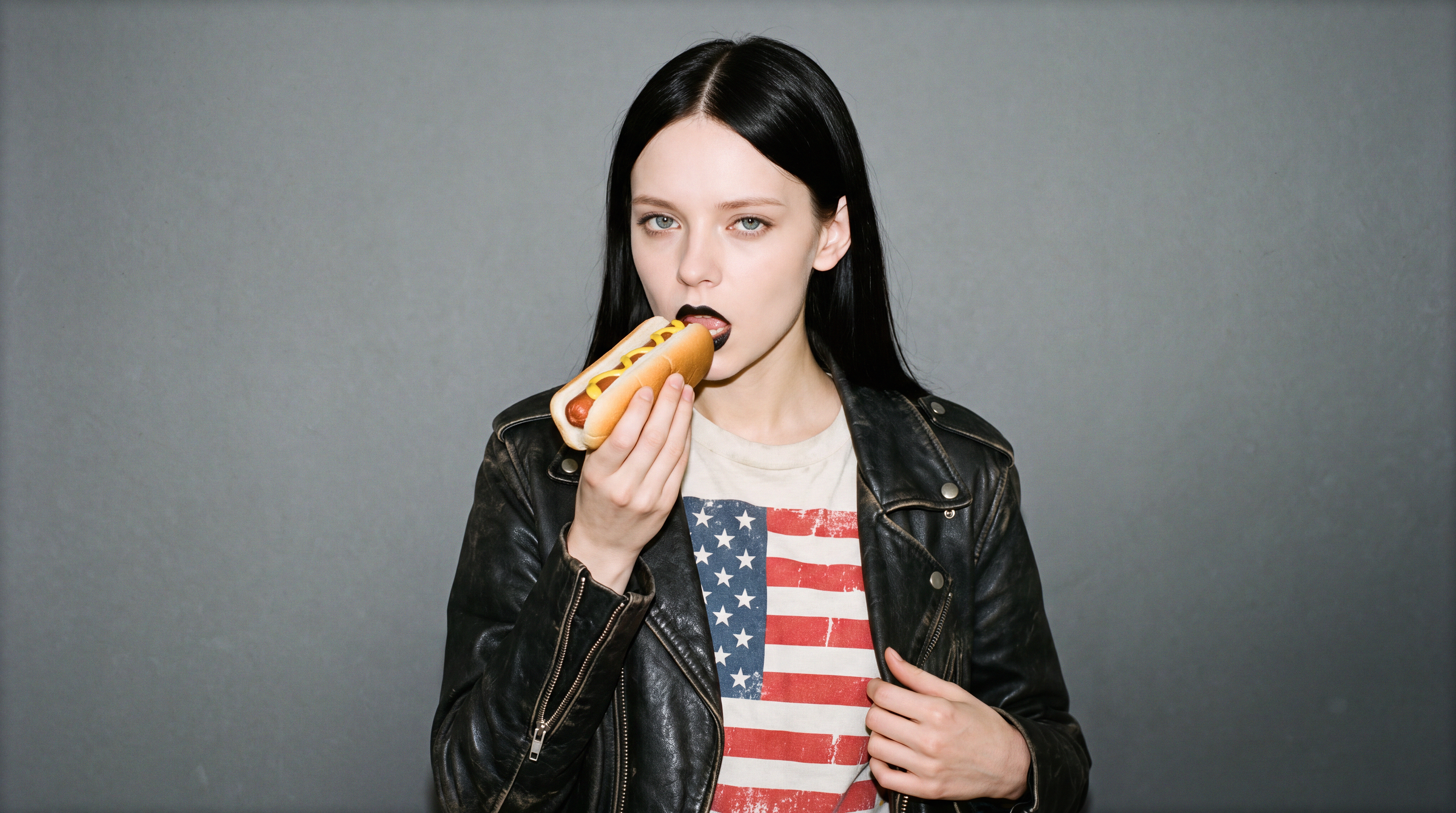 Editorial interview photograph of Marjorie Valentine wearing a shirt with American flag while eating a hot dog with standoffish expression.
