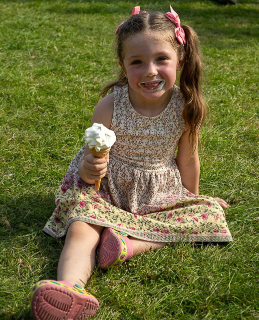 Black Country Boat Festival  - A young girl wearing a summer dress is sat on grass she has an ice cream in her hand and is smiling at the camera - Promo