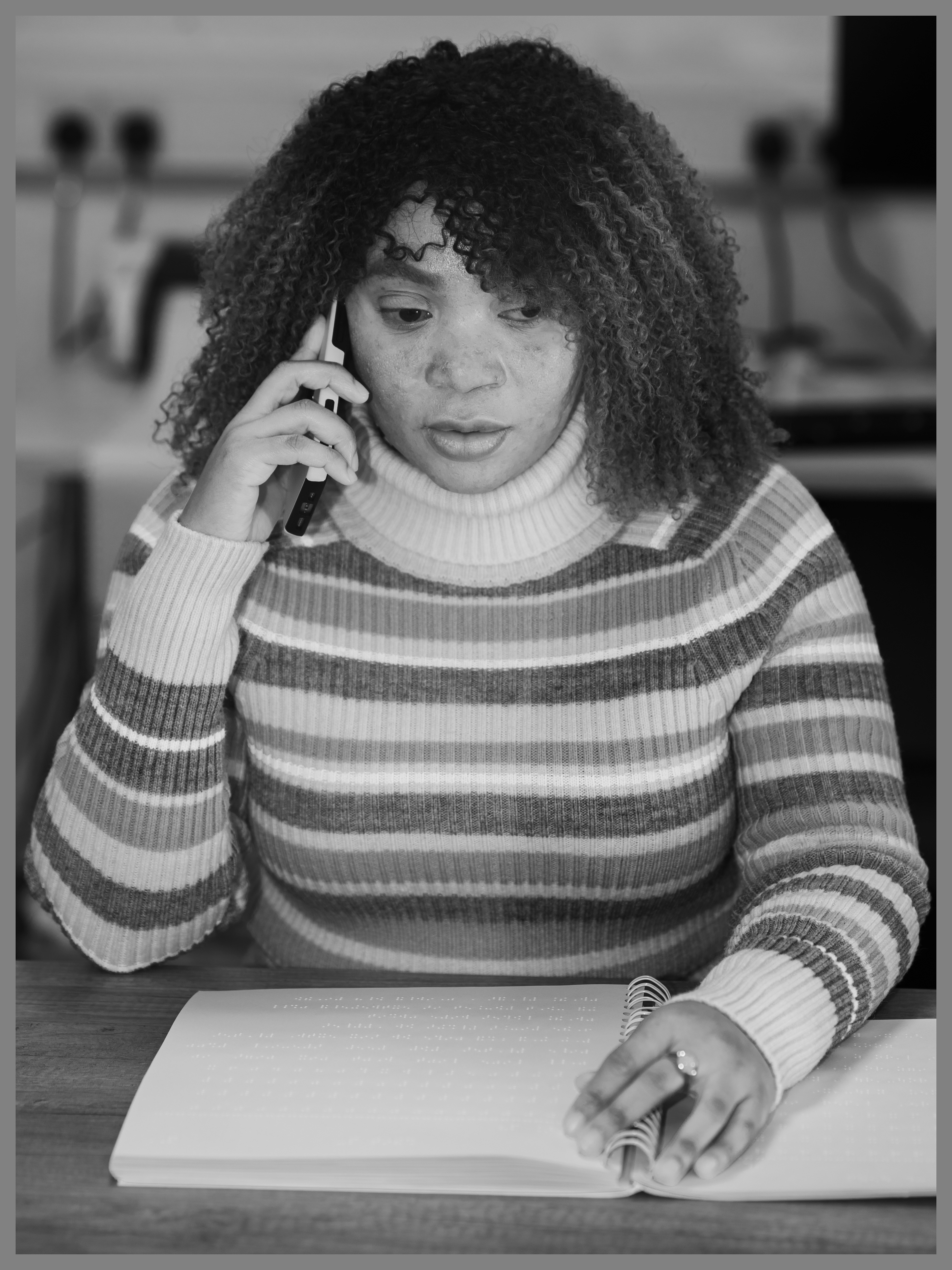 Peace - A young woman speaks on a mobile phone, her left hand is resting on an open book which is typed in braille